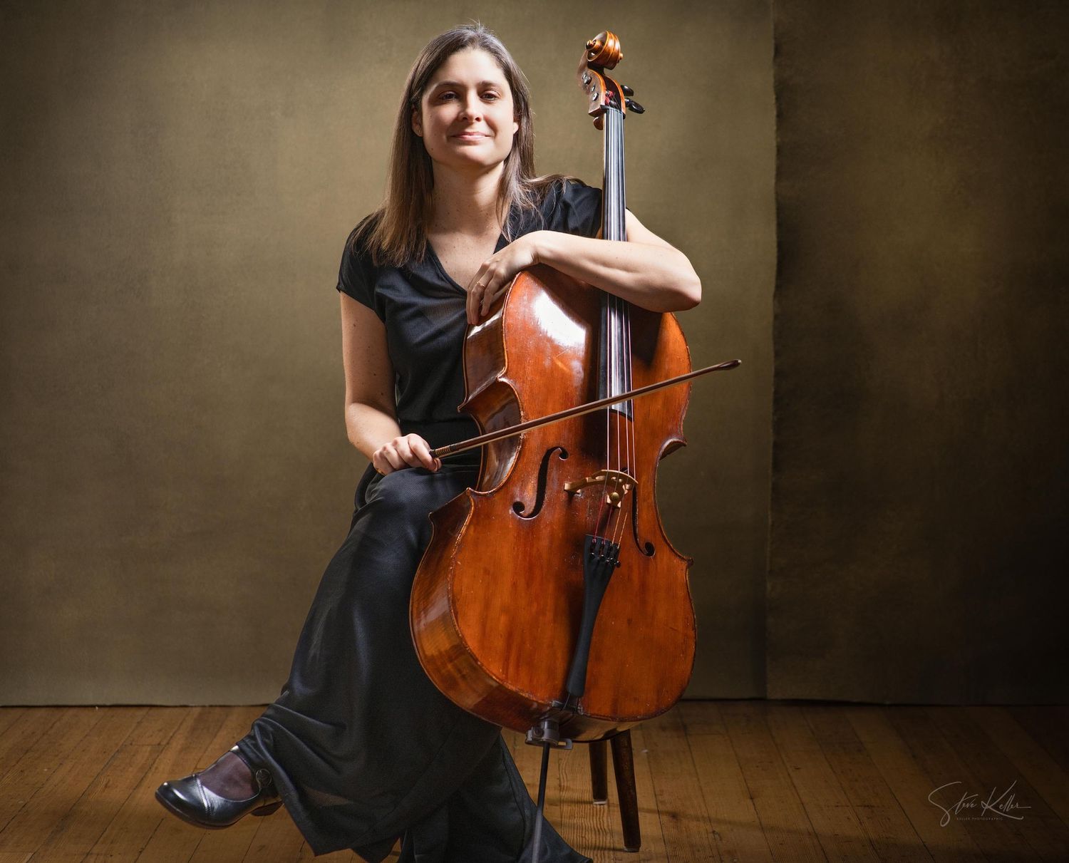 Professional cellist in a black dress performs with their wooden instrument against a dark textured background.
