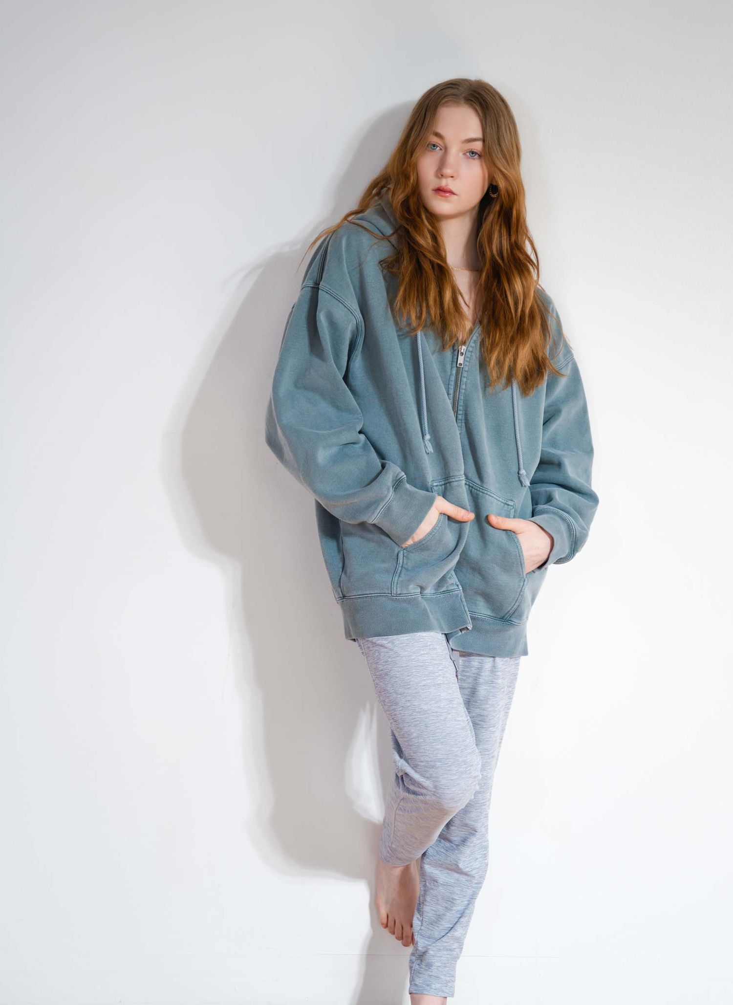 Model wearing an oversized blue-gray sweatshirt and light gray sweatpants poses against white backdrop in casual loungewear.