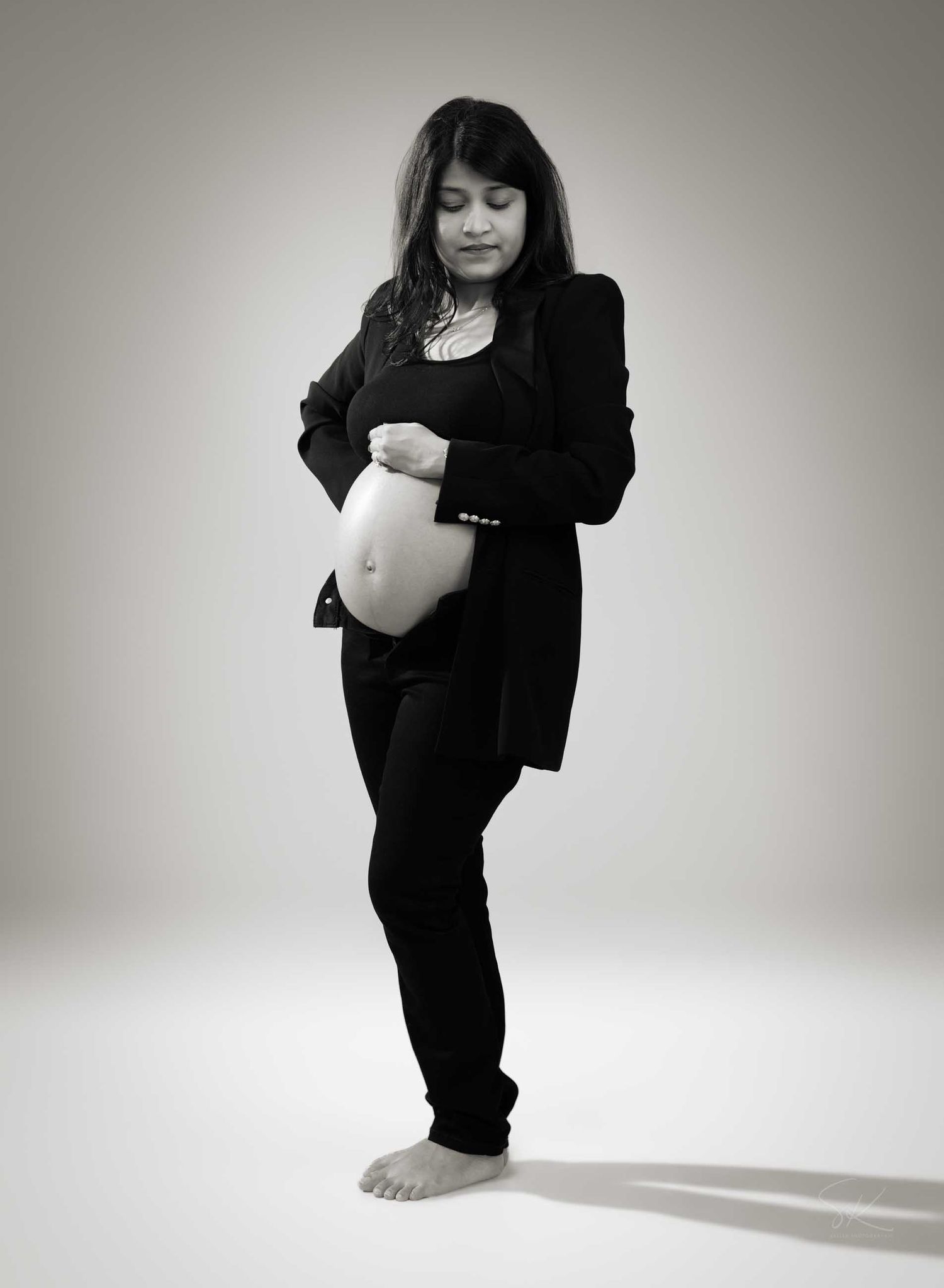 Black and white photo of a pregnant woman in black outfit cradling her baby bump while looking down tenderly.