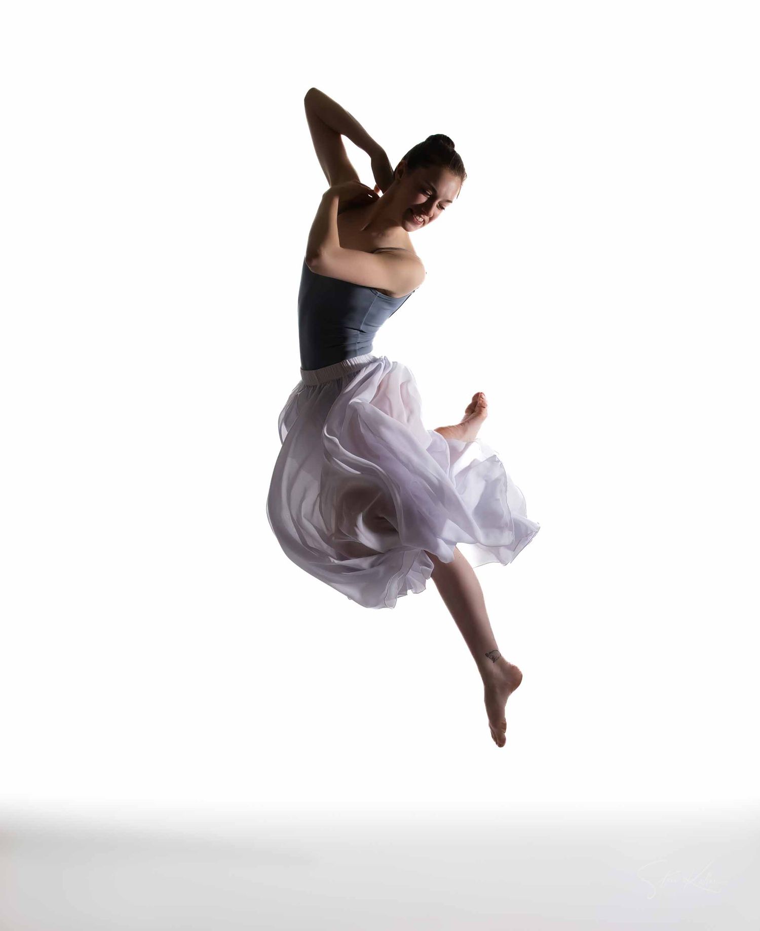 A dancer in a flowing white dress performs a graceful leap sequence against a light background.