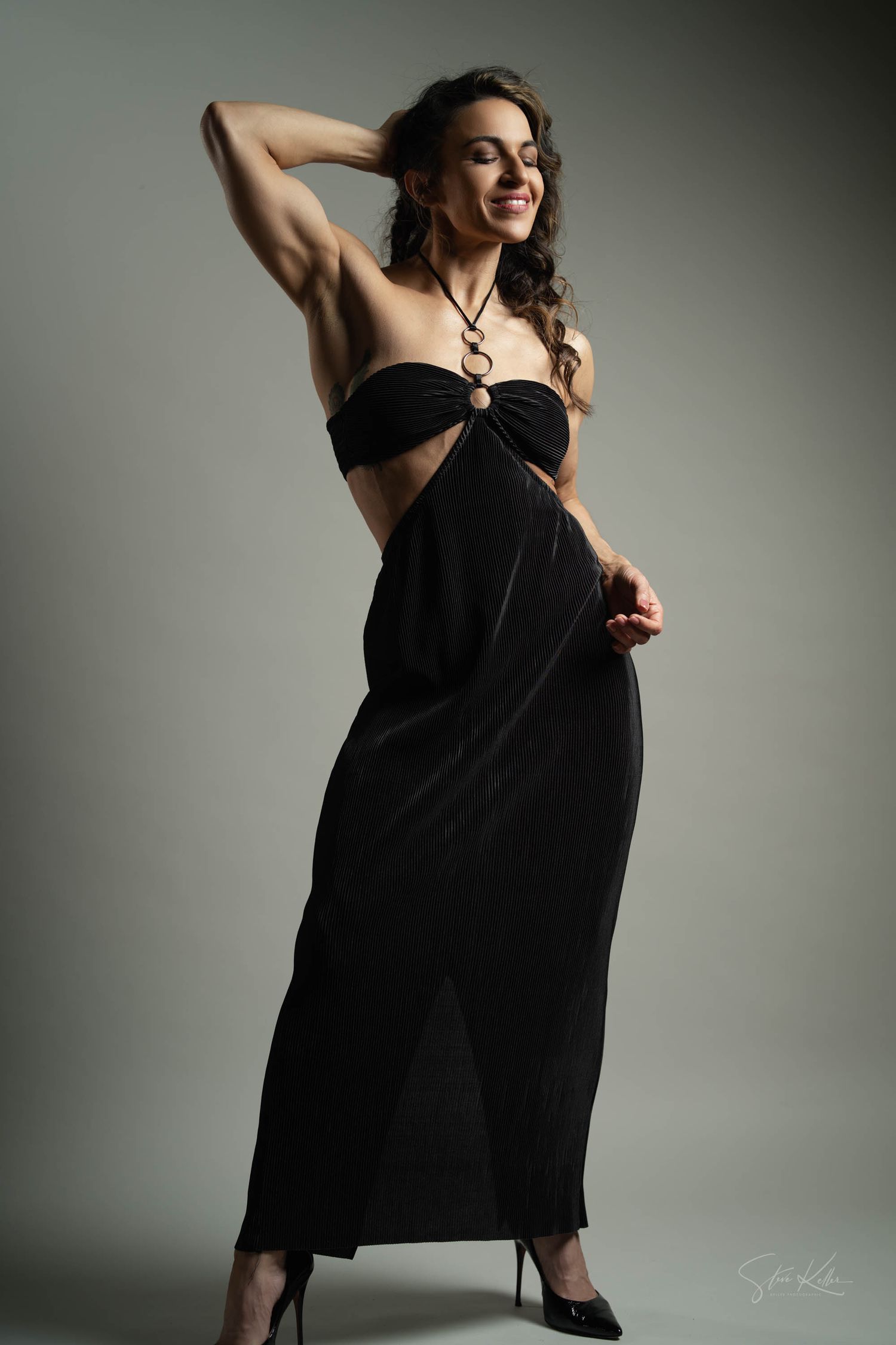 Glamour portrait of woman in black evening dress against gray backdrop.
