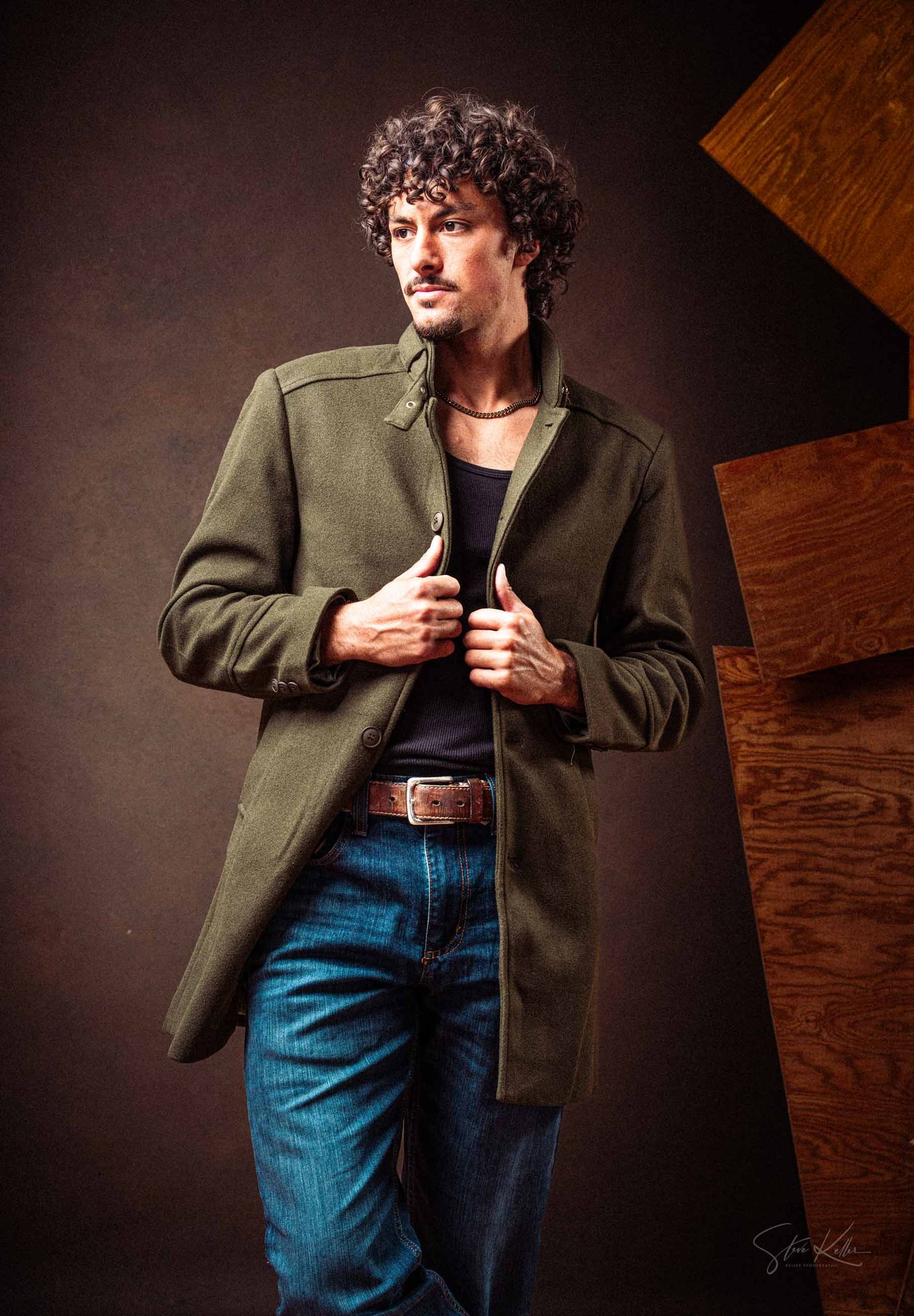 Model wearing green jacket and jeans strikes dramatic poses in moody studio lighting sequence.
