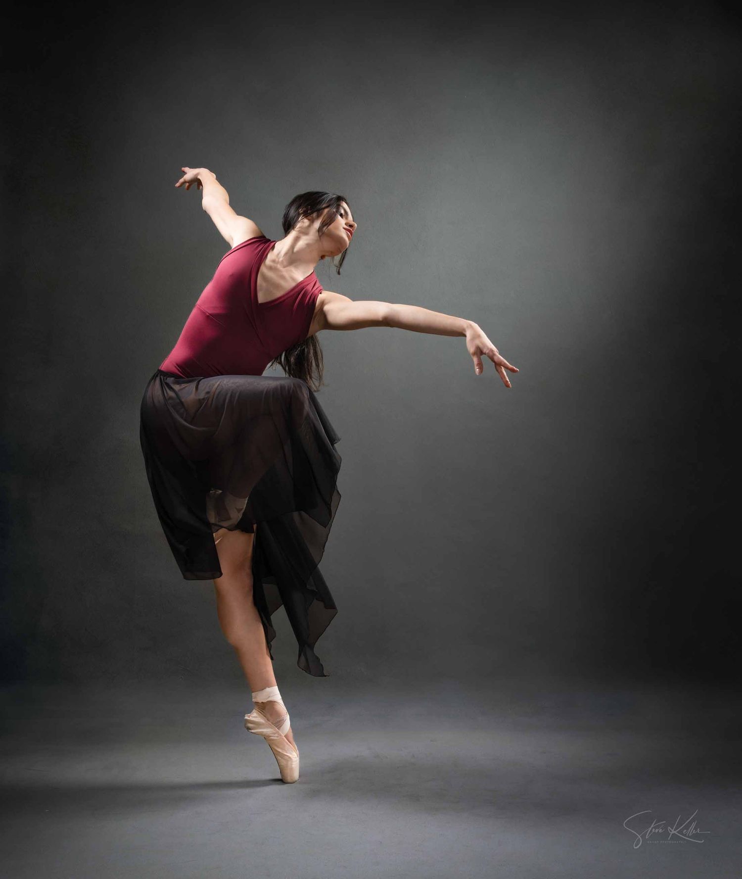 A dancer in burgundy leotard and black skirt performs a graceful sequence of modern dance movements against a dark backdrop.