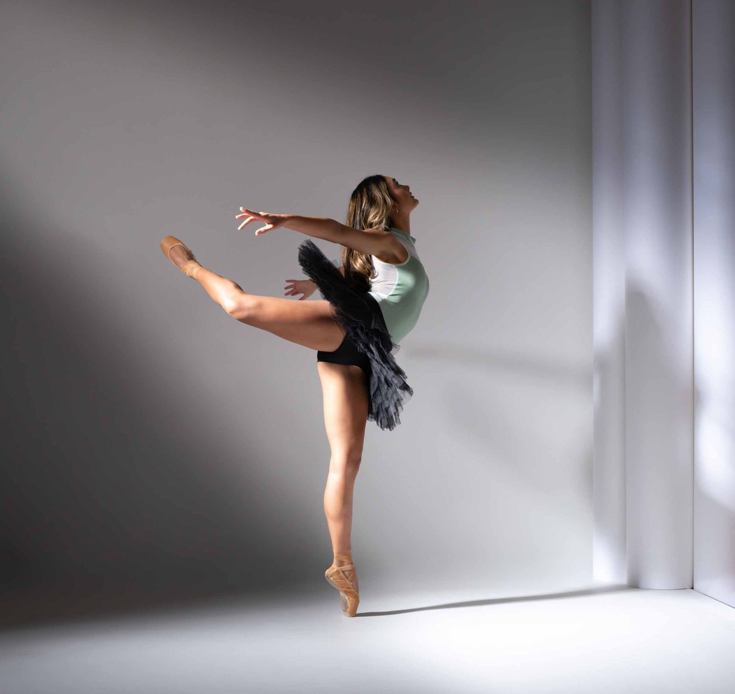 Ballet dancer performs graceful movements in white tutu against minimalist grey studio backdrop.