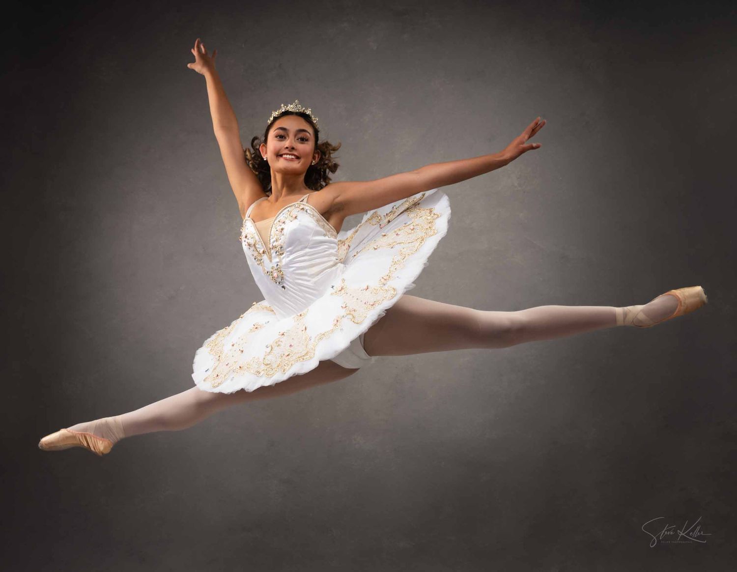 Graceful ballet dancer in white tutu performs dynamic split leap sequence against dark studio backdrop.