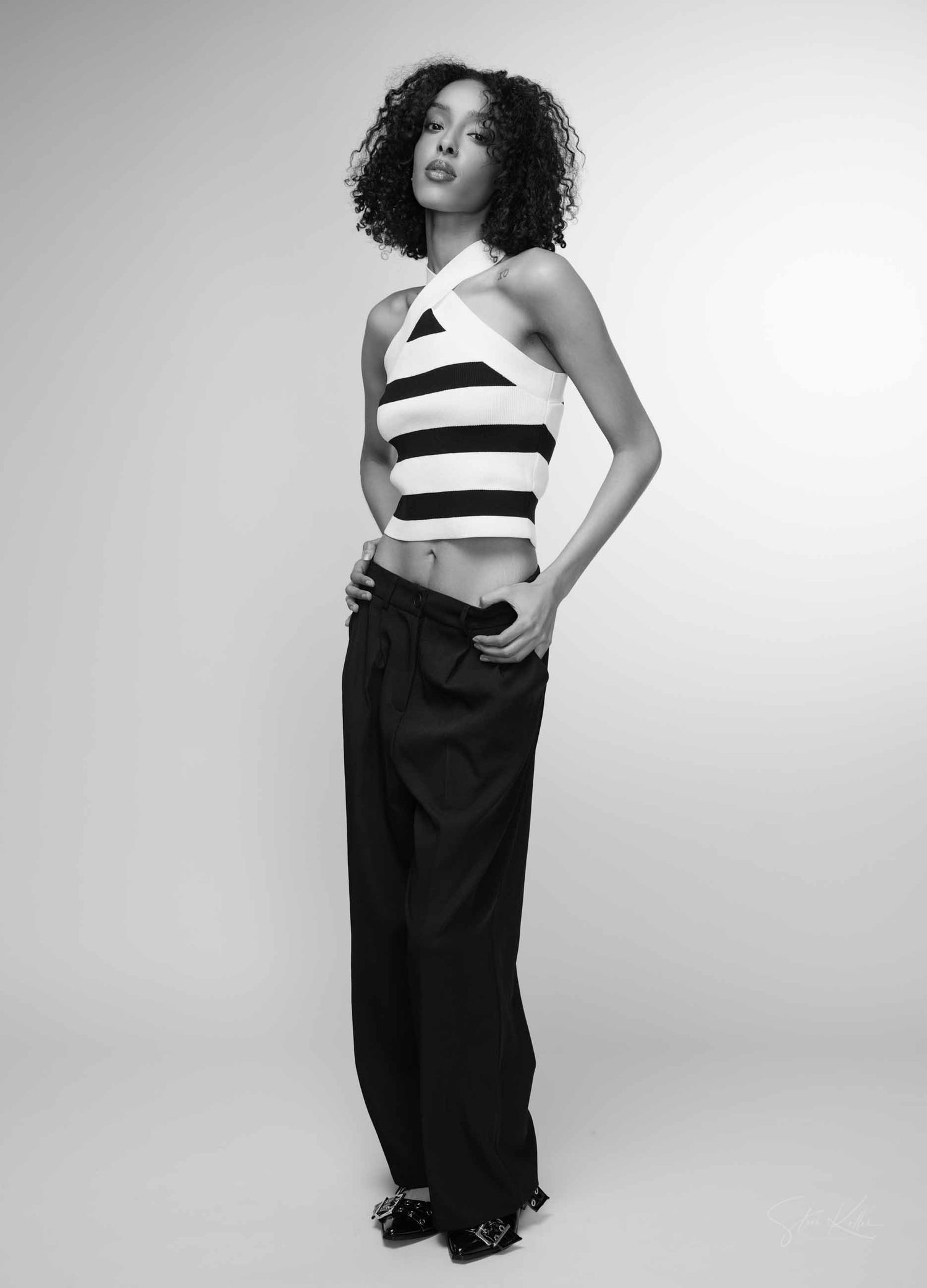 A fashion model poses in a black and white striped halter top and flowing black skirt against a light background.