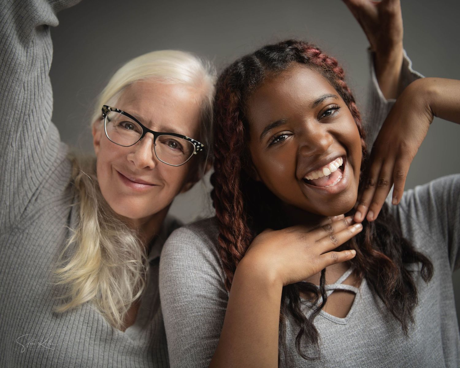 Two people posing playfully with bright smiles in a warm studio portrait.