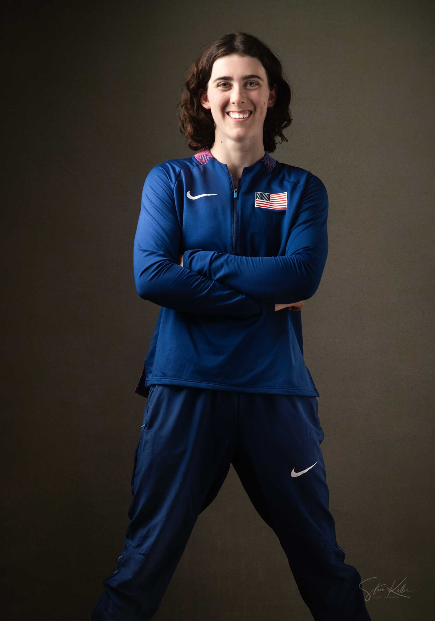 Athletic figure in navy blue Nike sportswear poses against dark background in professional studio portraits.