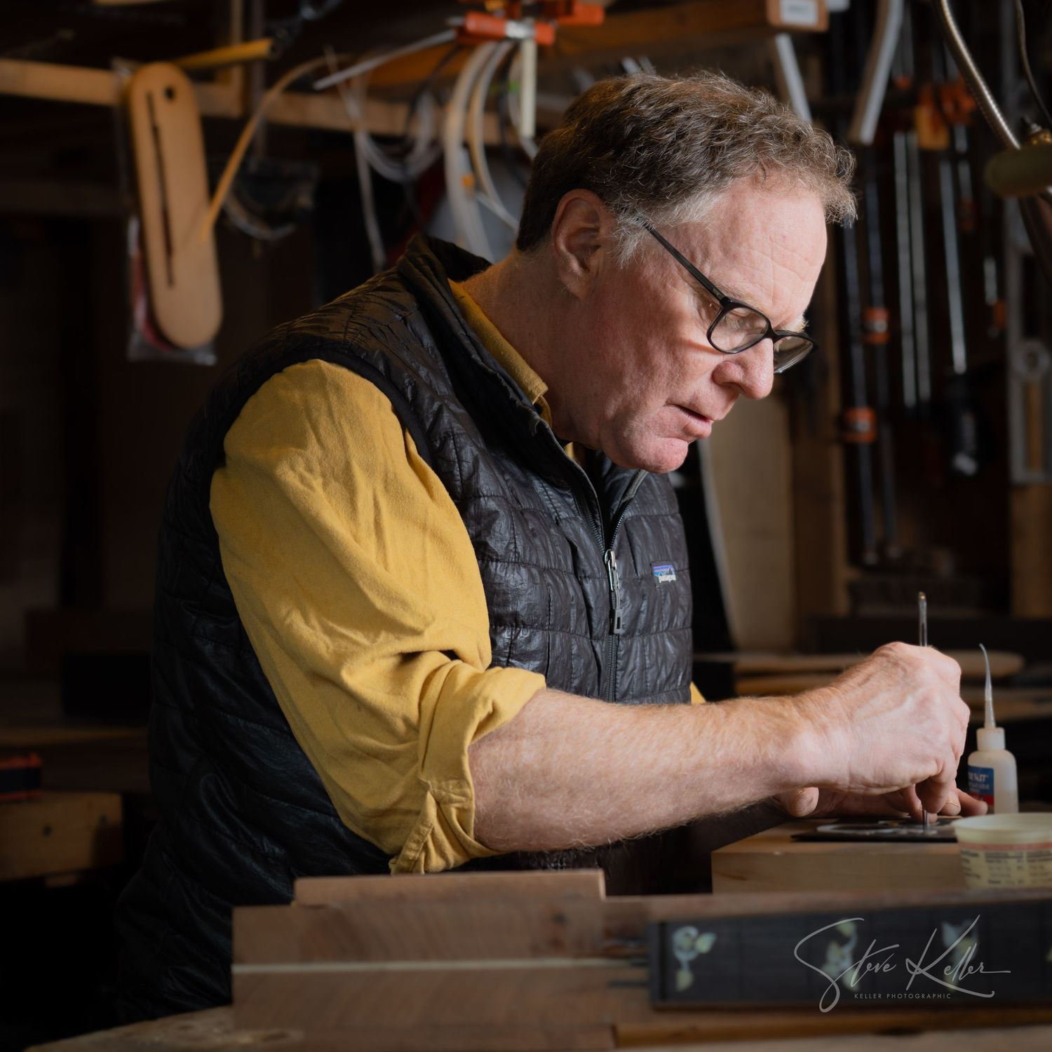 Craftsperson wearing yellow sleeves and dark vest working intently on detailed project.