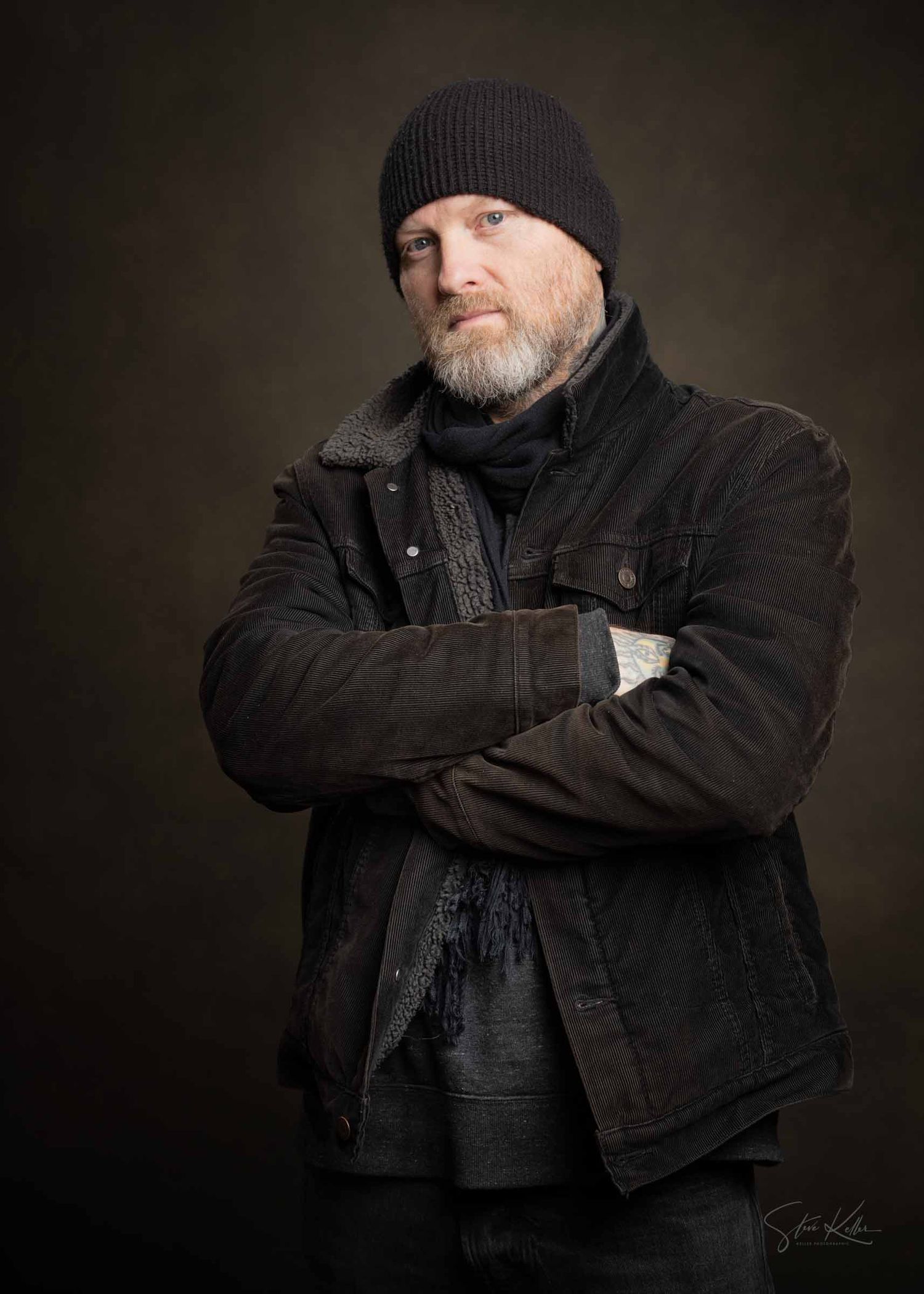 A person wearing a black beanie and dark jacket poses against a dark background in a dramatic studio portrait series.