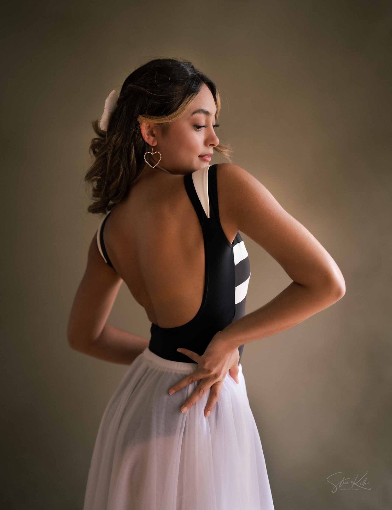 A ballet dancer in a flowing white and black dress strikes an elegant pose against a dark background.