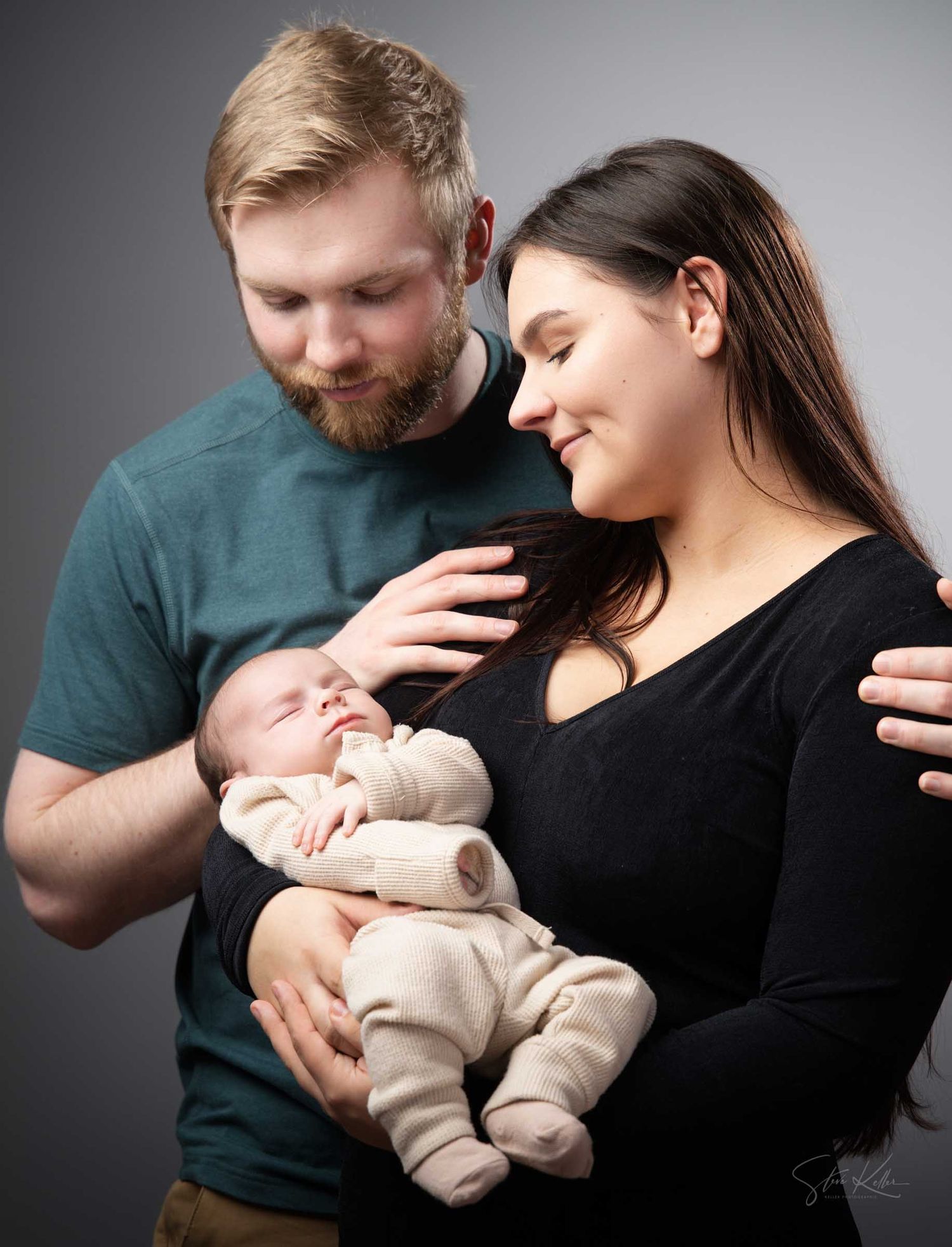 A couple tenderly gazes at their newborn baby during a professional studio portrait session.