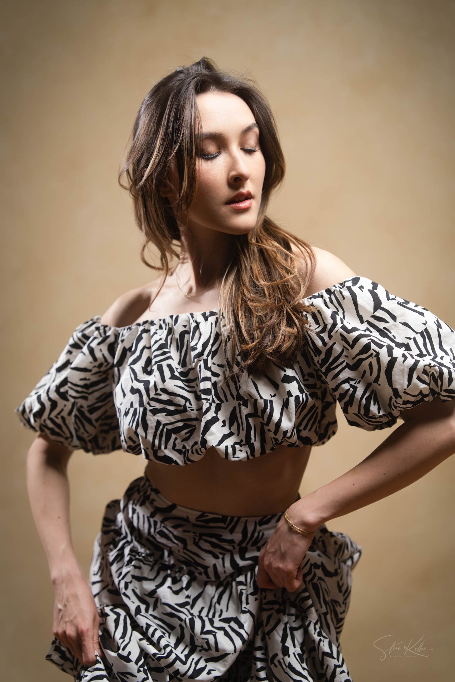 Fashion model poses in black and white patterned off-shoulder dress with ruffled details against beige backdrop.