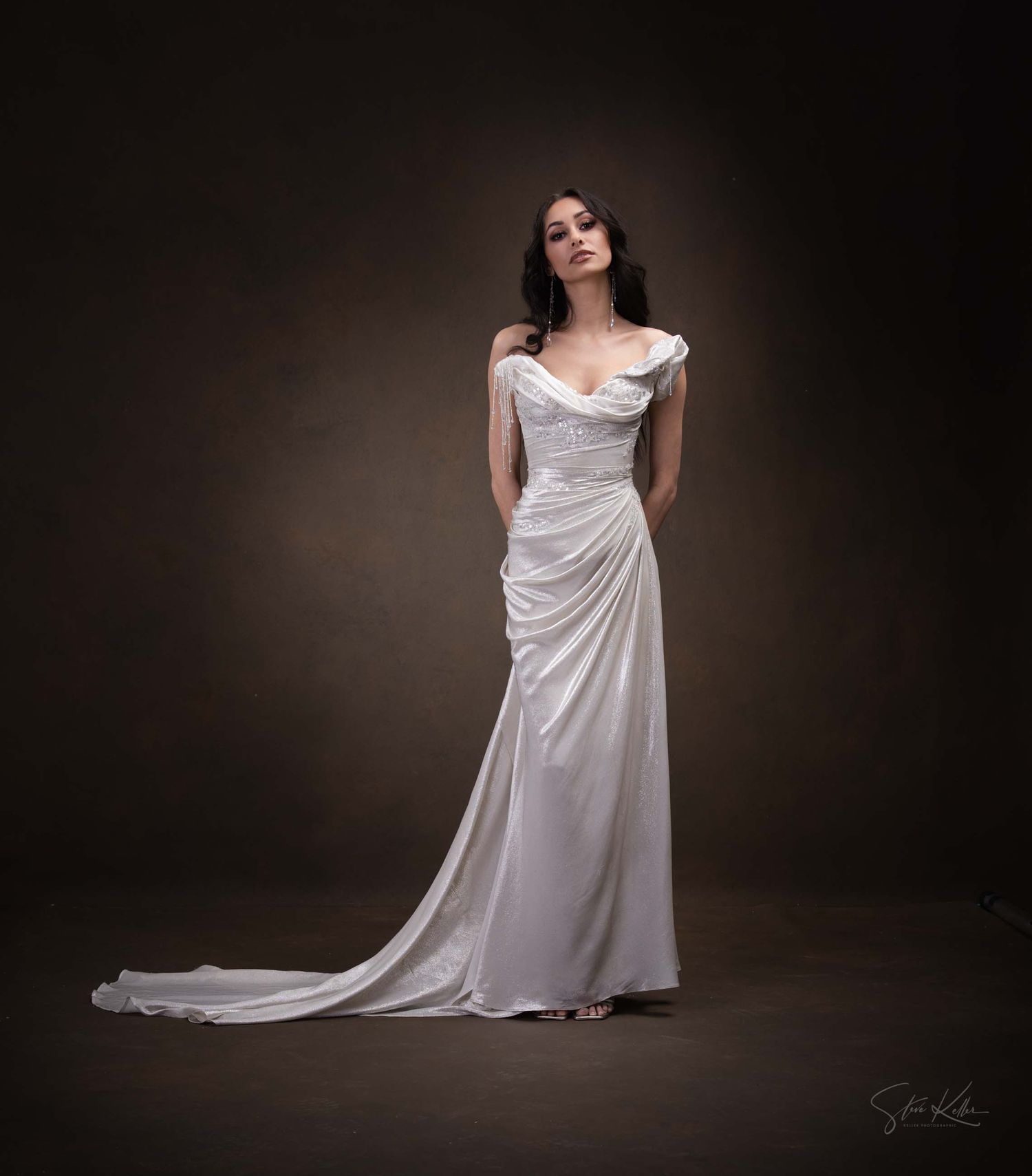 Elegant white satin wedding gown with flowing train photographed against dark studio backdrop.