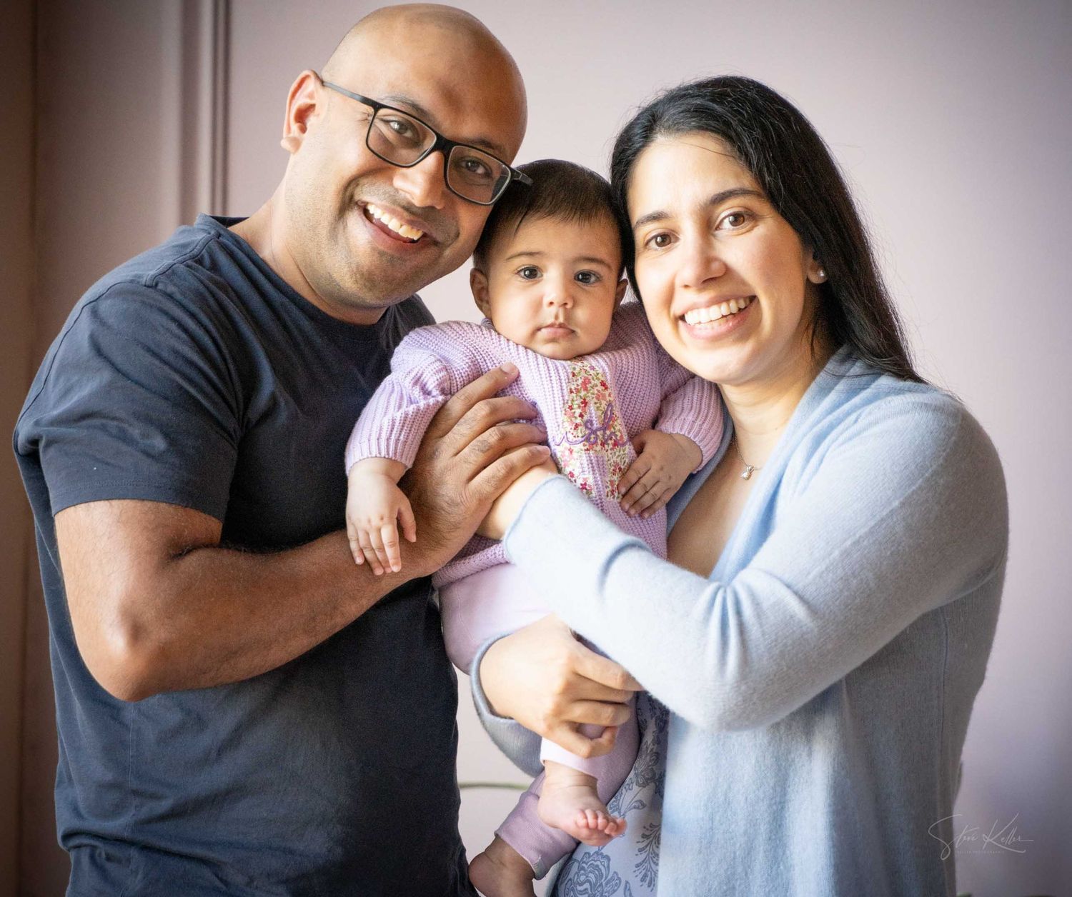 Happy family portrait with parents smiling and holding their baby girl dressed in pink.
