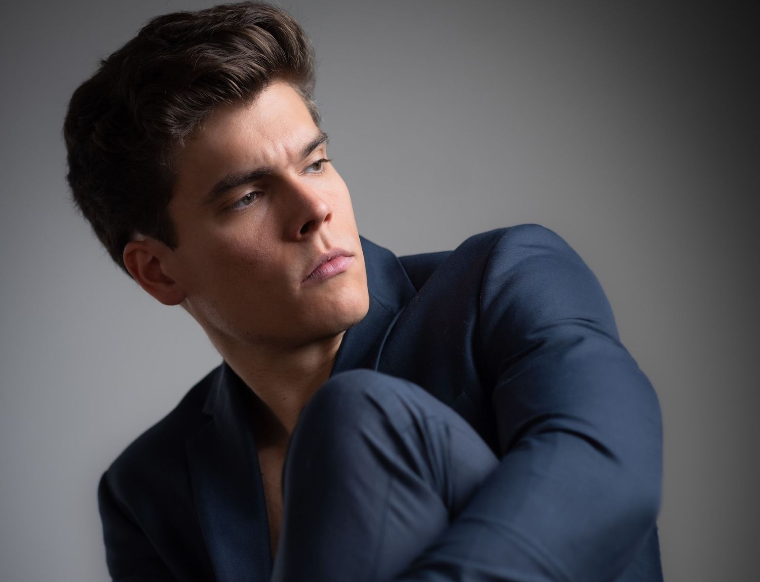 Professional studio portrait of someone in a navy blue shirt looking to the side.