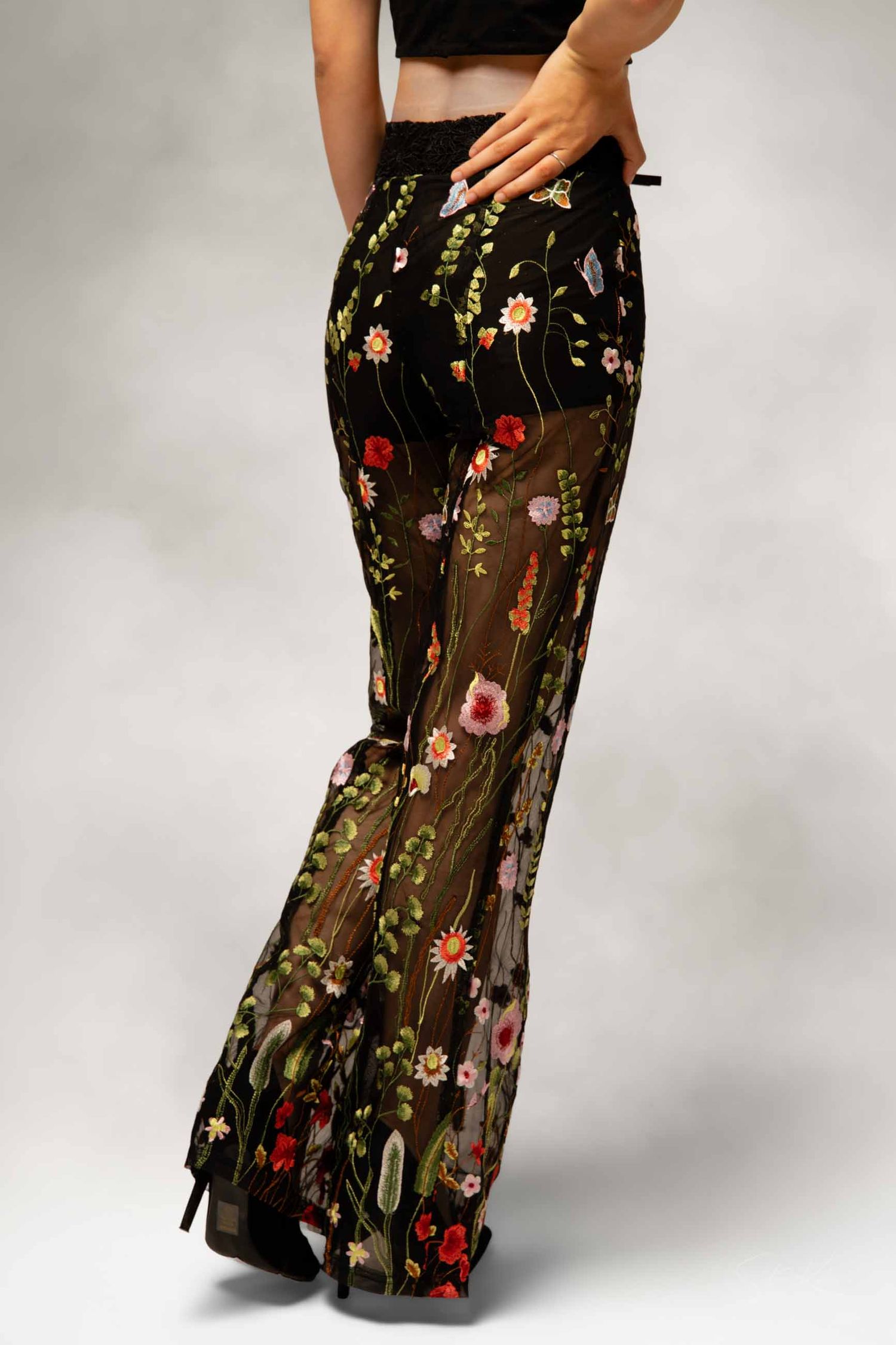 Close-up of black sheer floral embroidered flare pants with delicate flower details and high heels.