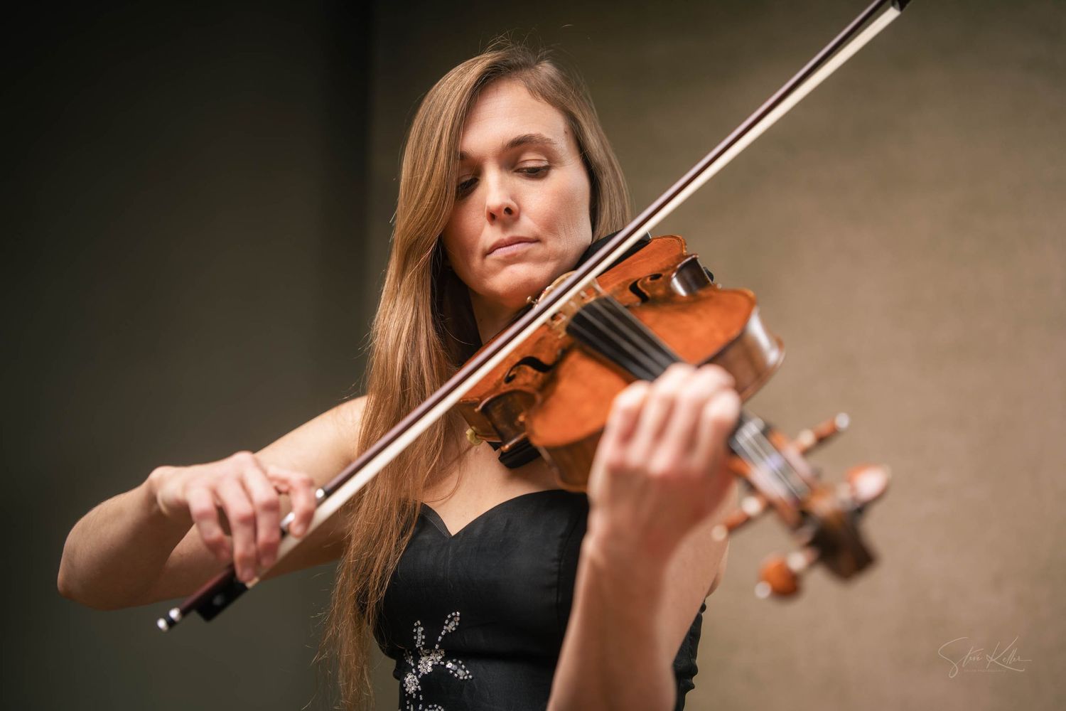 A violinist performs with focused intensity while playing classical music on a wooden violin against a neutral background.