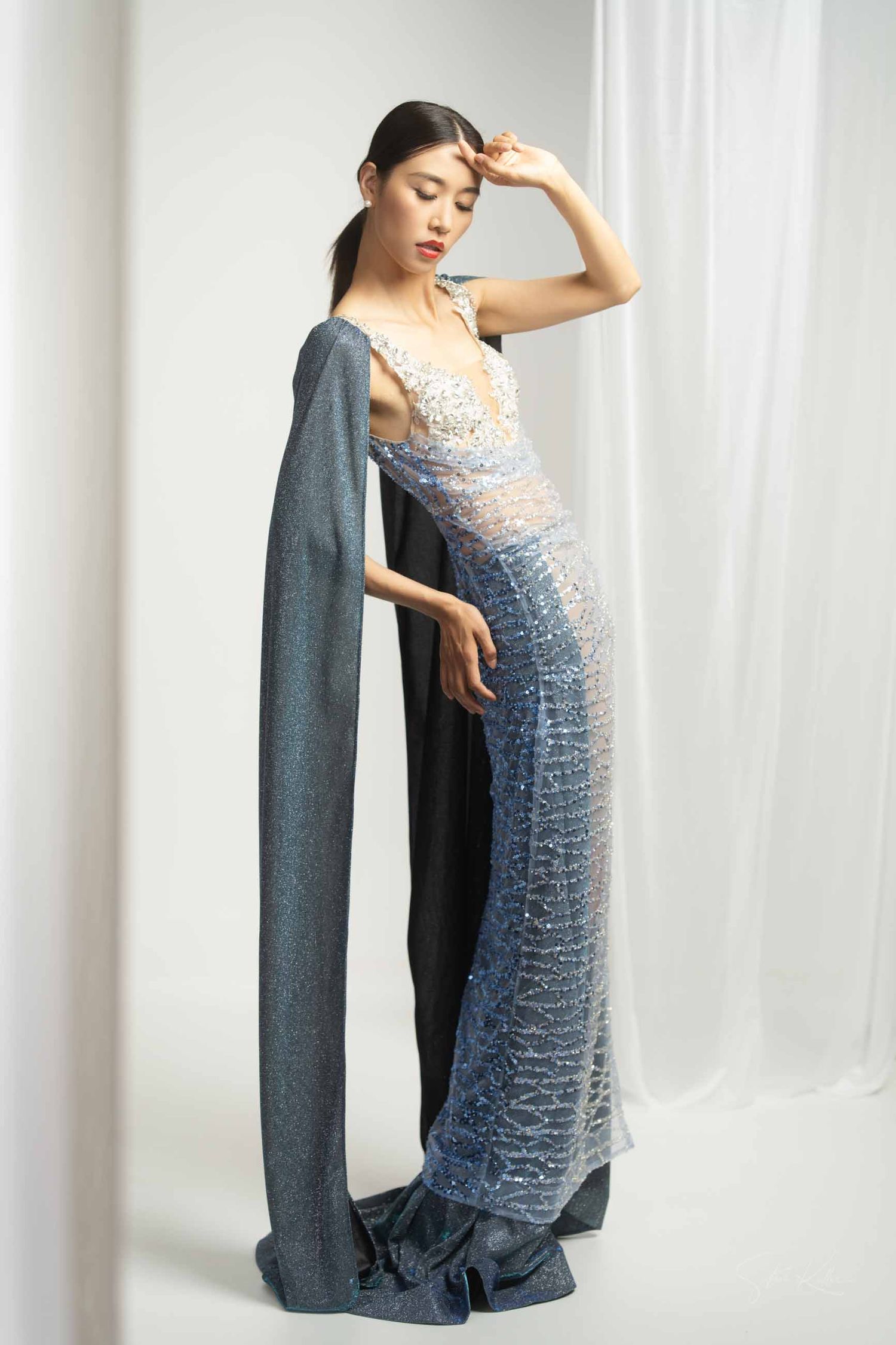 Artistic maternity photoshoot featuring a grey strapless dress and long draped cardigan against white backdrop.