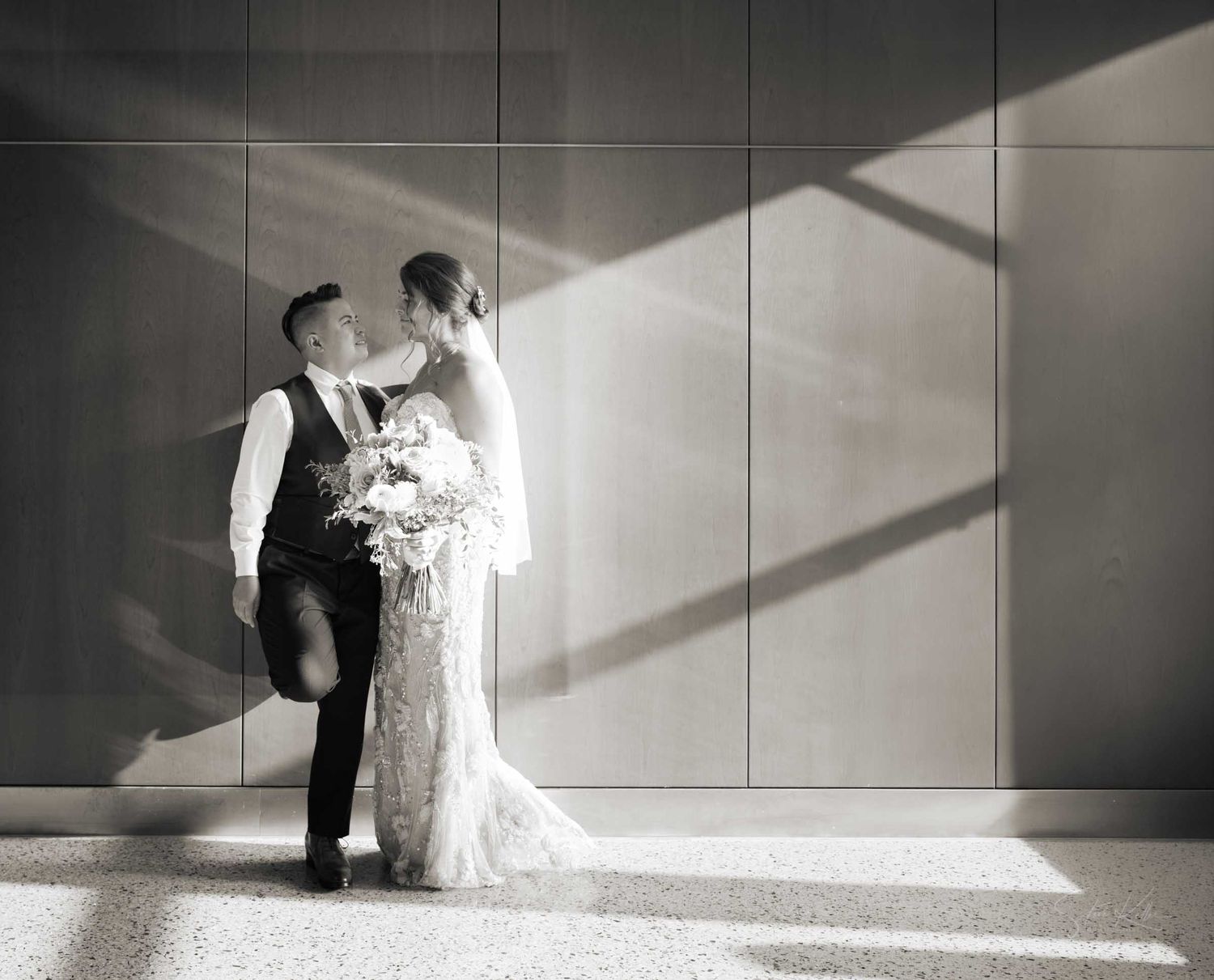 Bride and groom sharing a romantic kiss in black and white wedding portrait with dramatic light shadows.