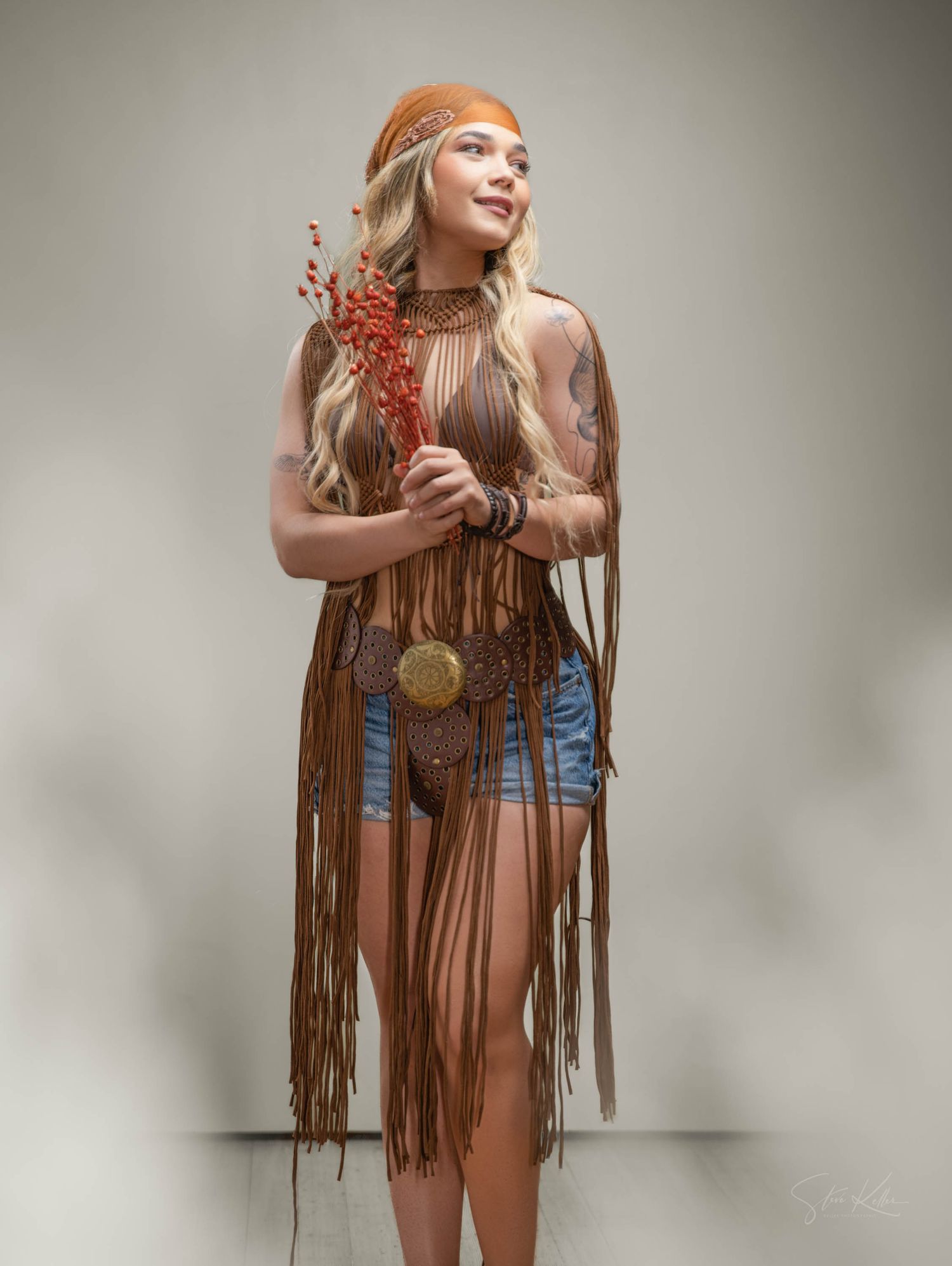 Bohemian fashion model in fringe dress holds red berries against light studio background.