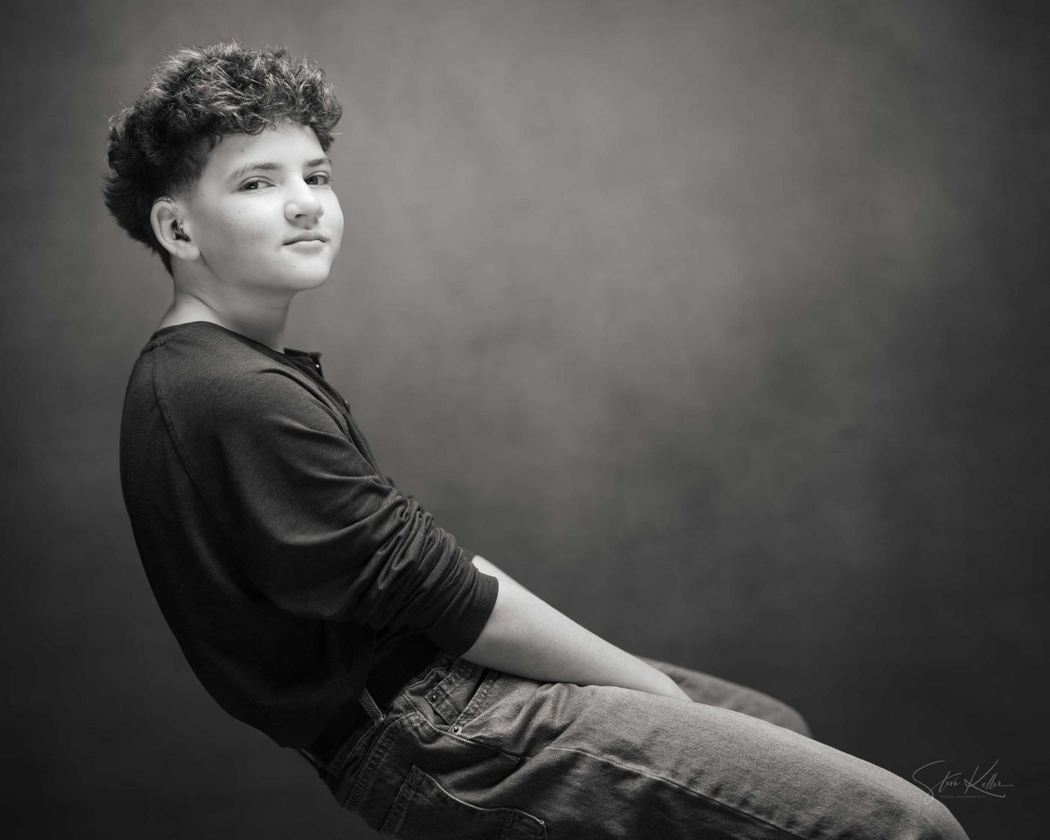 Black and white portrait of a young person with curly hair posing confidently in casual clothing against a studio backdrop.