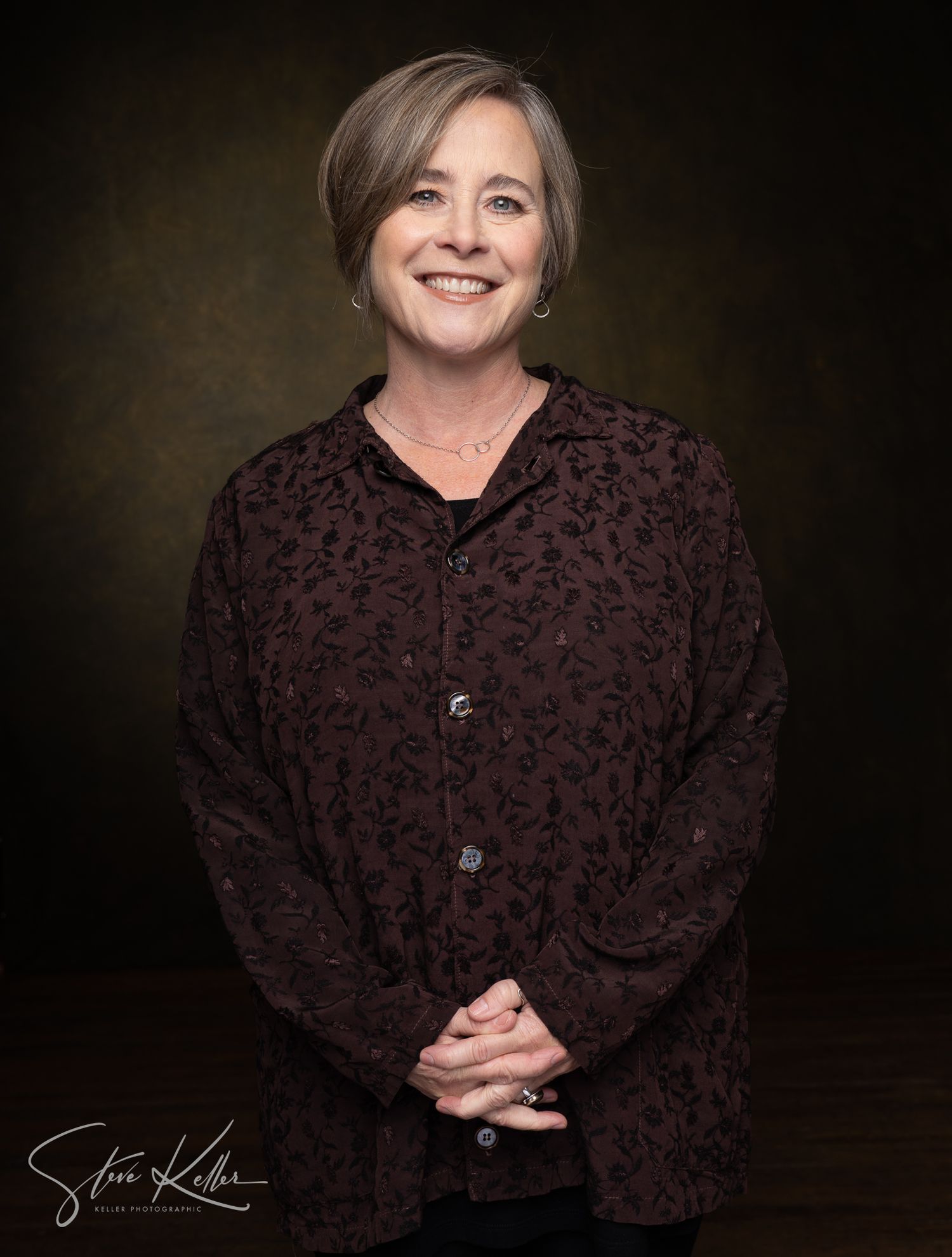 Portrait of woman in dark textured button-up shirt against brown background.