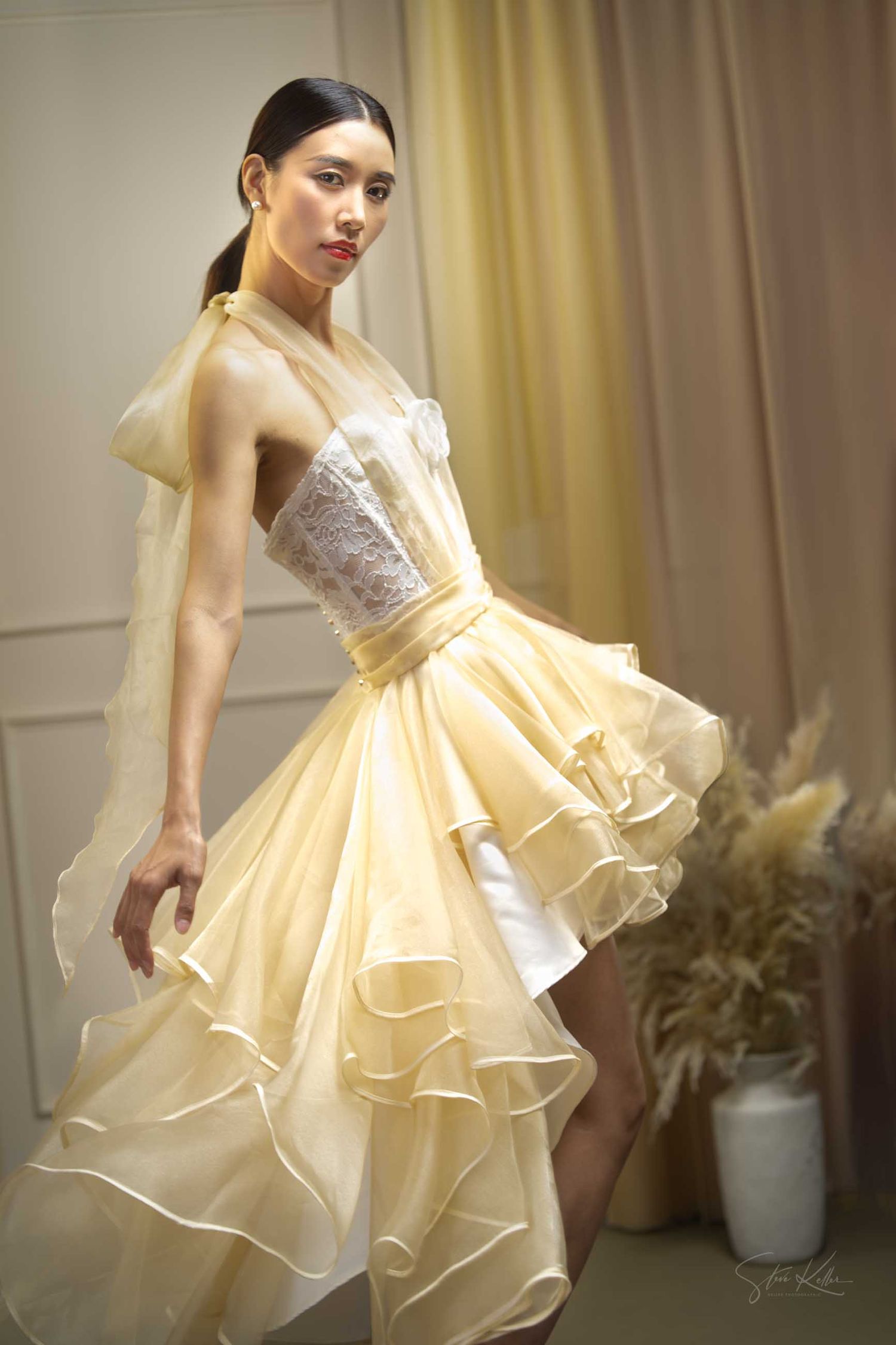 A ballet-inspired photoshoot featuring a short ruffled dress in warm cream tones against a curtained backdrop.