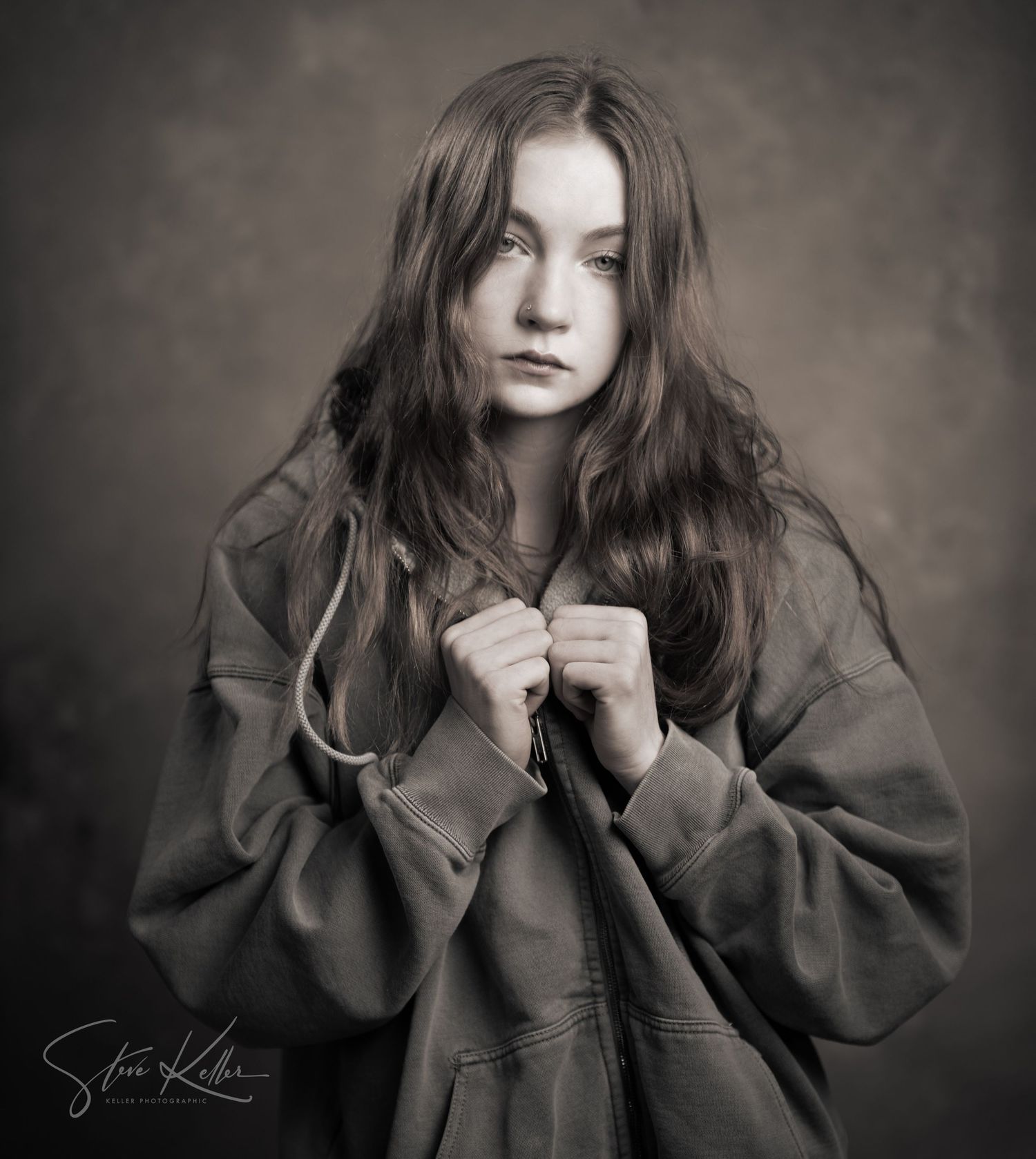 Dramatic portrait showing oversized grey coat against moody dark background.