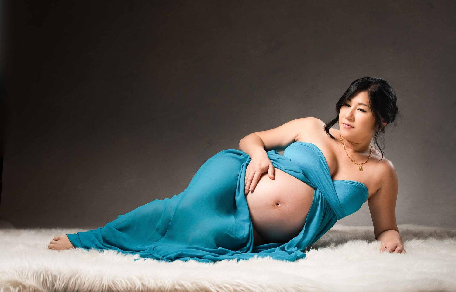 Maternity photo series showing a woman in a teal dress posing gracefully on a white backdrop.