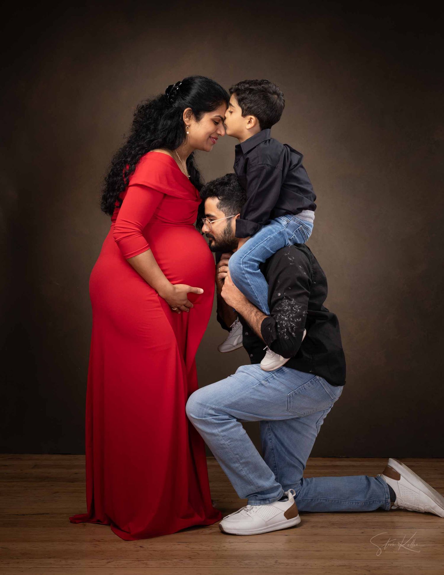 A person in a red dress and another in denim and black jacket share an intimate moment in a dark studio setting.