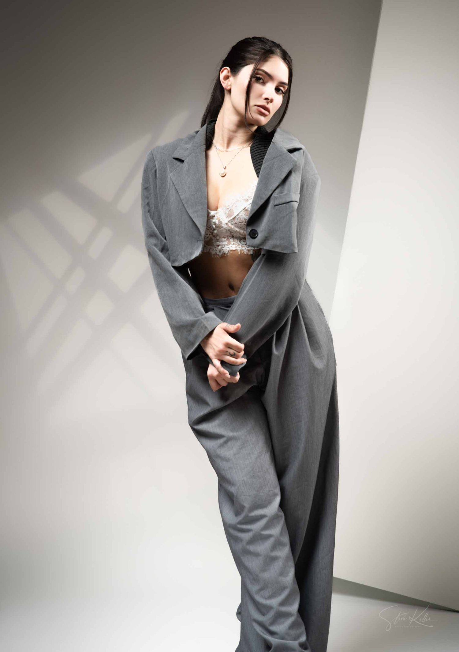 Model poses in an oversized grey blazer and silver sequined top against a neutral studio background.