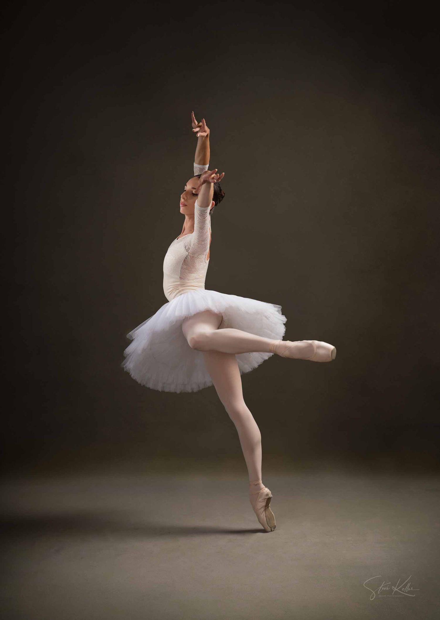 A ballet dancer in a white tutu performs an elegant sequence of graceful movements on a dark stage.
