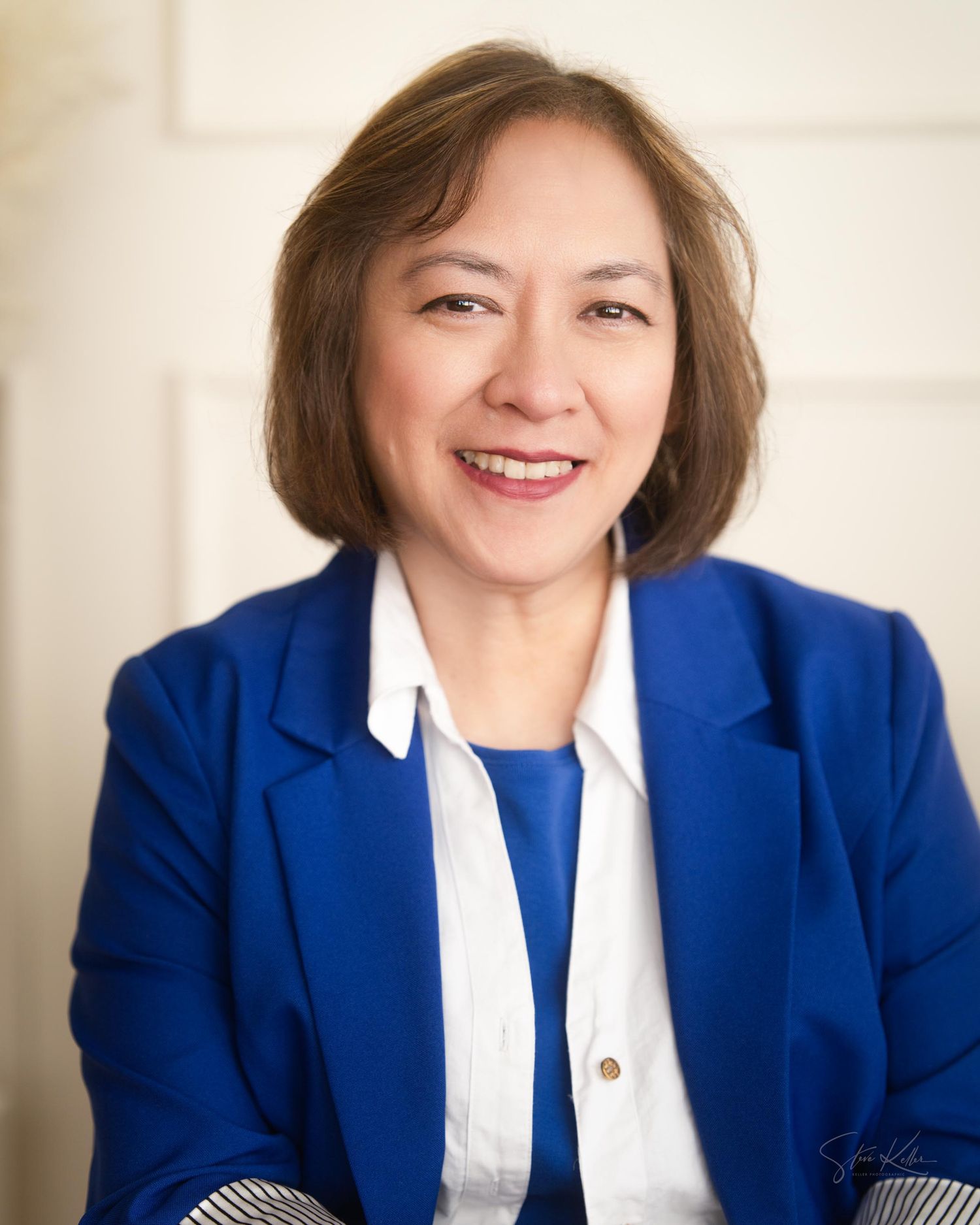 Professional portrait of a person in a bright royal blue blazer and white collared shirt against a light background.
