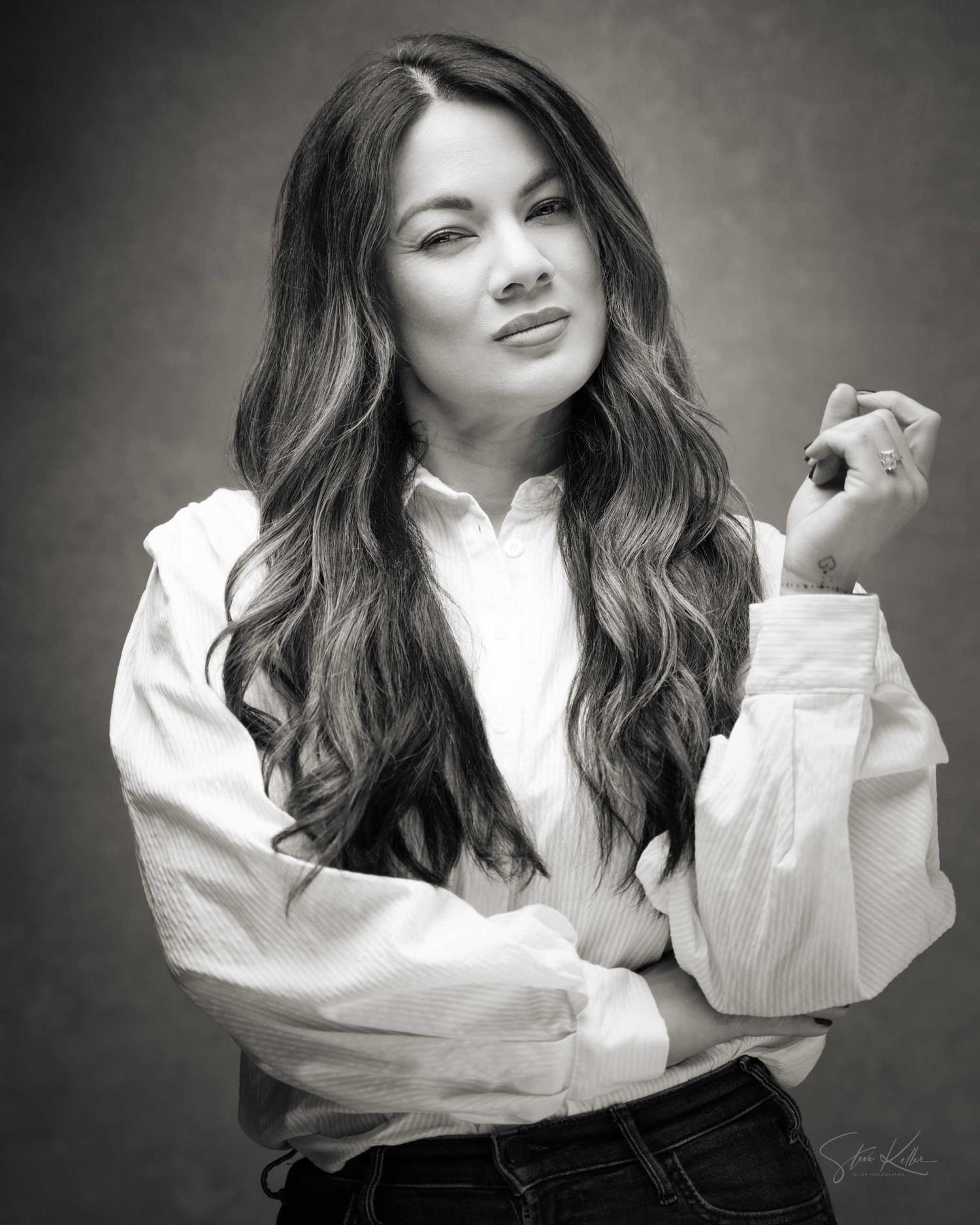 Black and white portrait of a woman with long wavy hair wearing a white blouse, posing confidently.