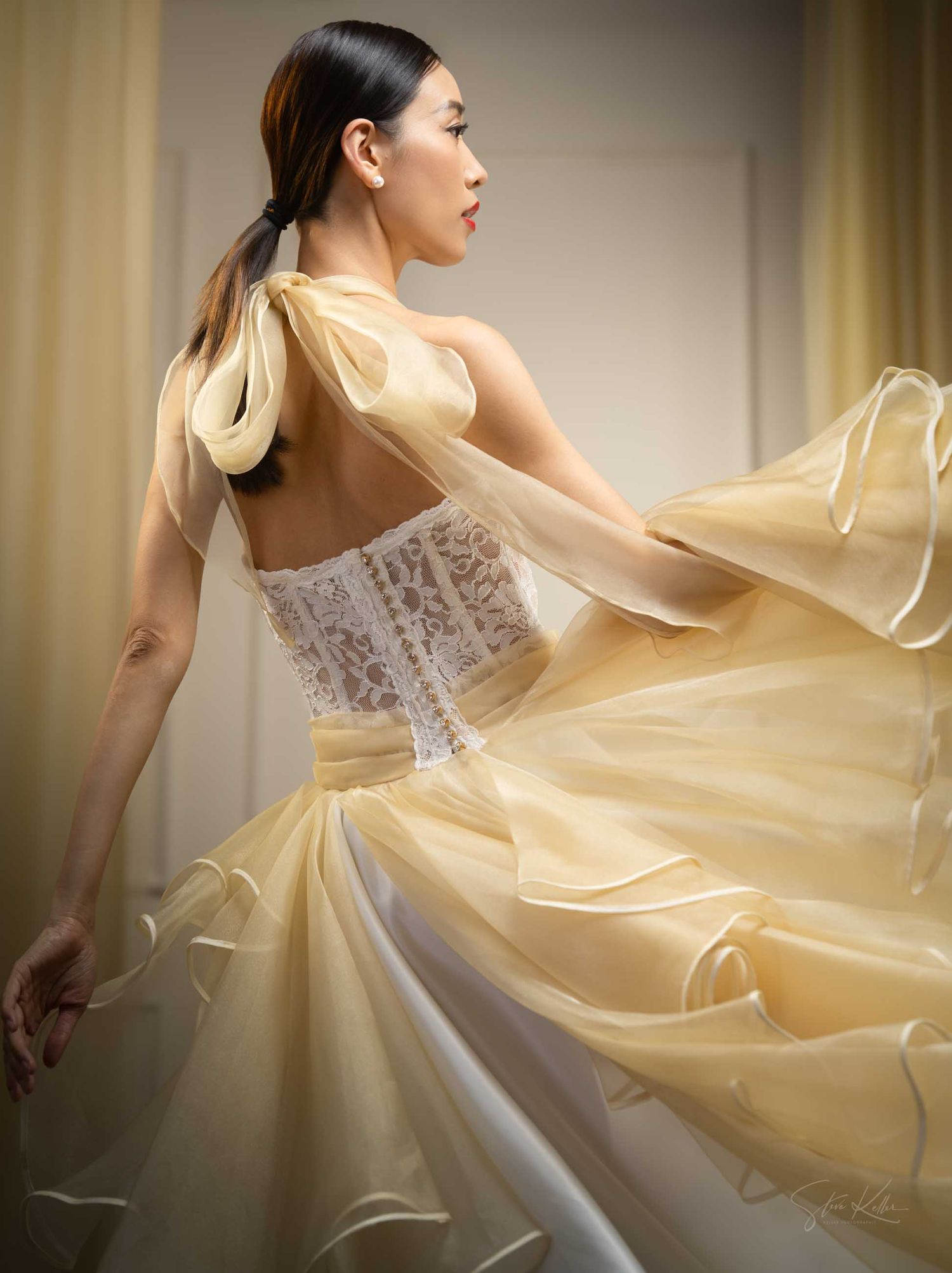 Elegant white dress with fitted bodice and billowing sheer overlay photographed in soft ambient lighting.