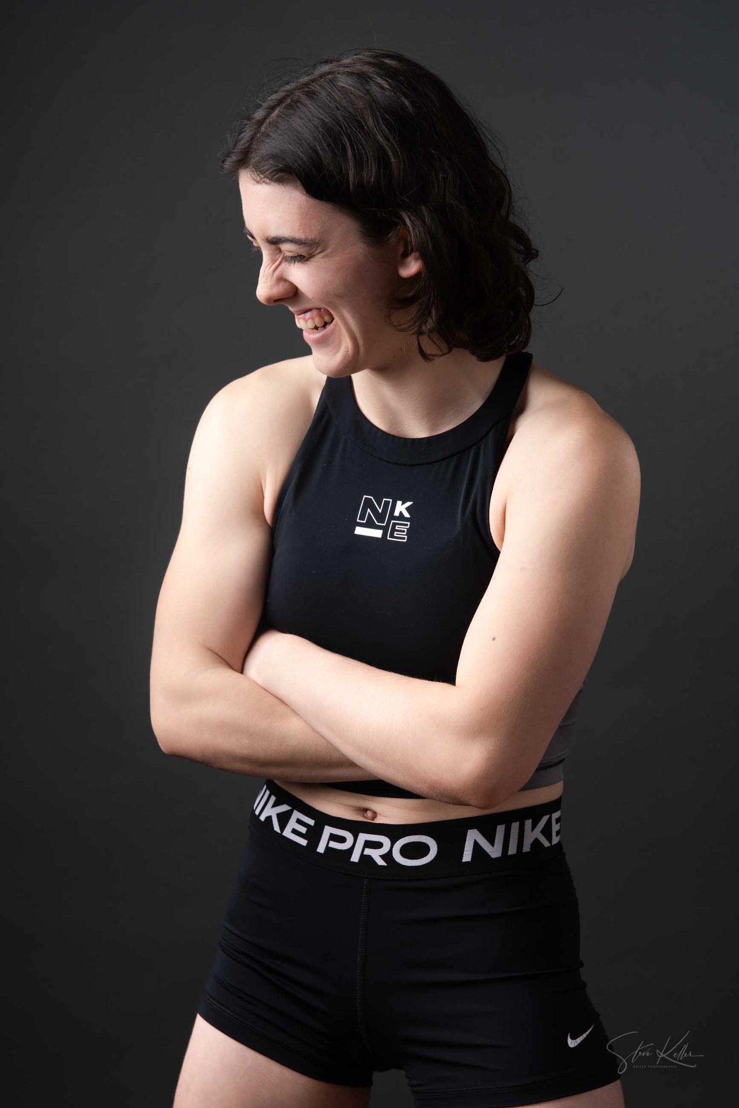 Fitness model in black Nike Pro sports wear poses against dark backdrop in studio lighting.