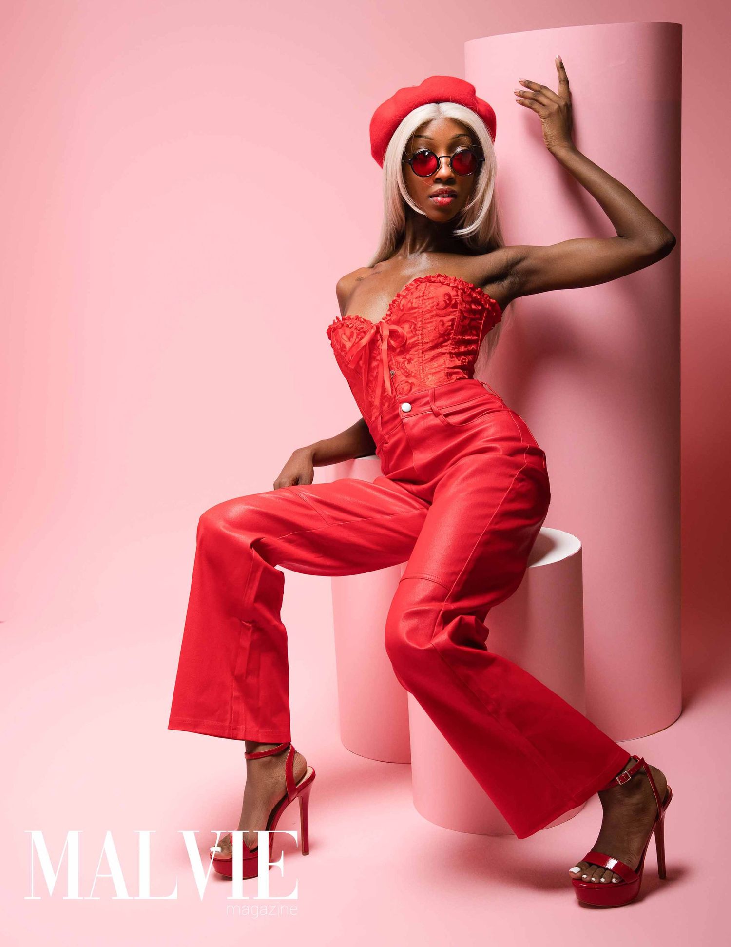 Fashion model in vibrant red jumpsuit poses elegantly against pink backdrop in dynamic editorial photoshoot series.