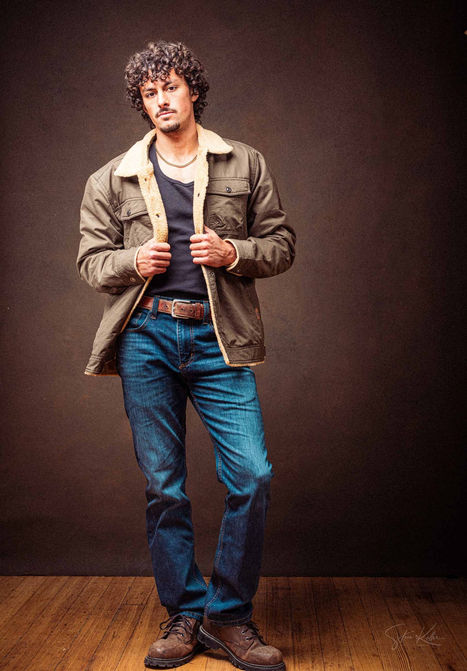 Person in casual outfit with brown jacket and blue jeans strikes dynamic poses against dark background on wooden floor.