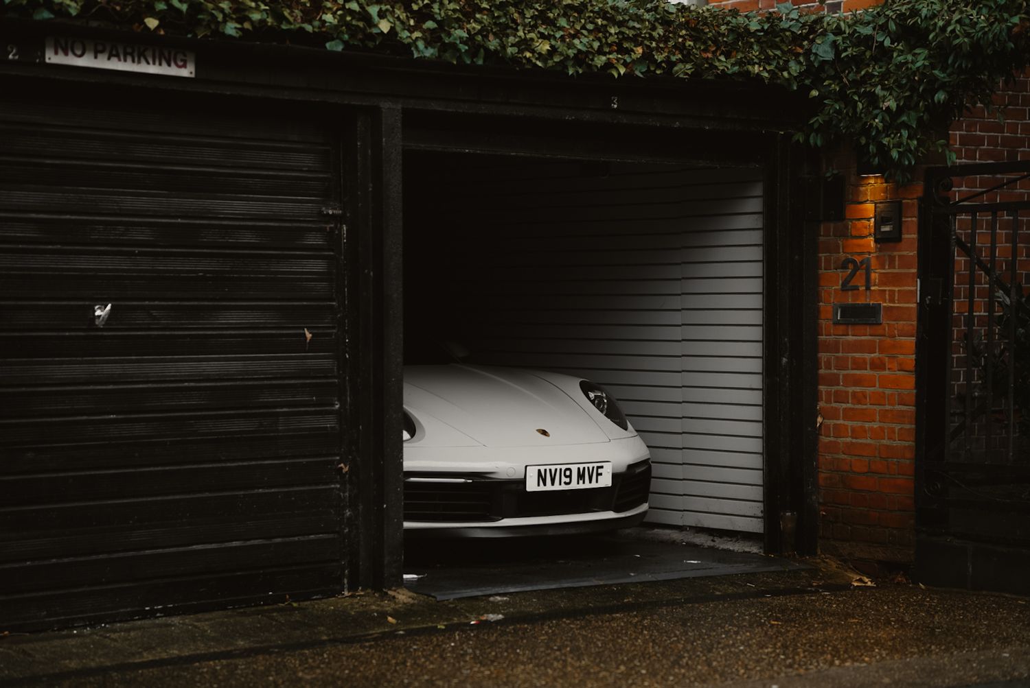 A sleek sports car partially visible inside a dark garage with brick walls and ivy.