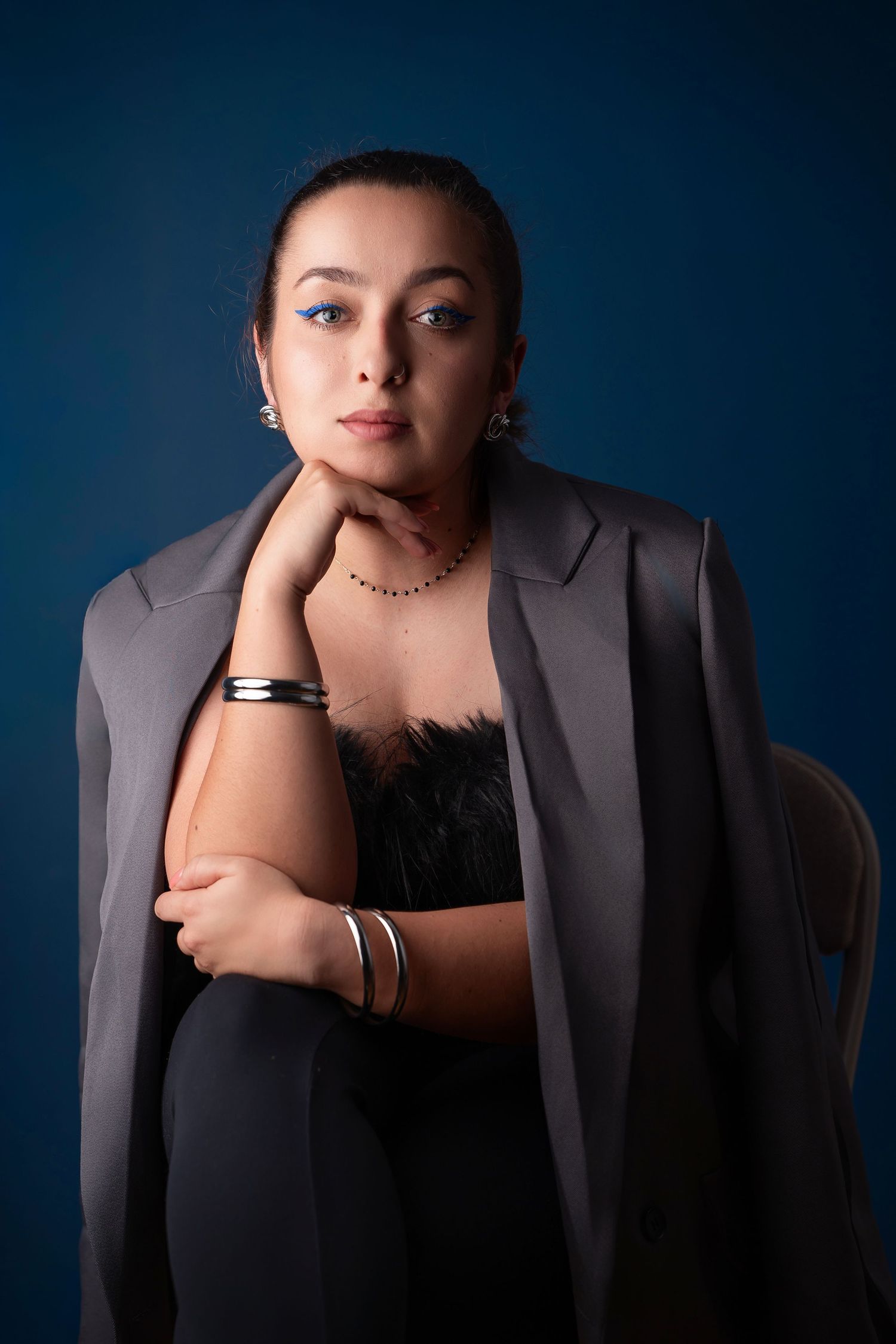 Professional studio portrait with moody lighting features a person in a gray blazer and black top against a deep blue background.