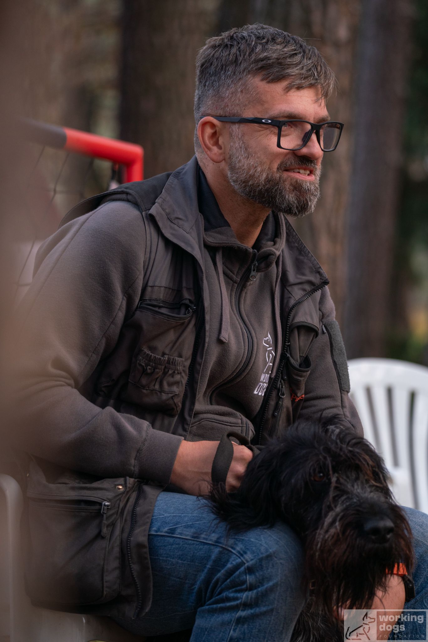 Person in casual attire sitting outdoors with a small black dog.