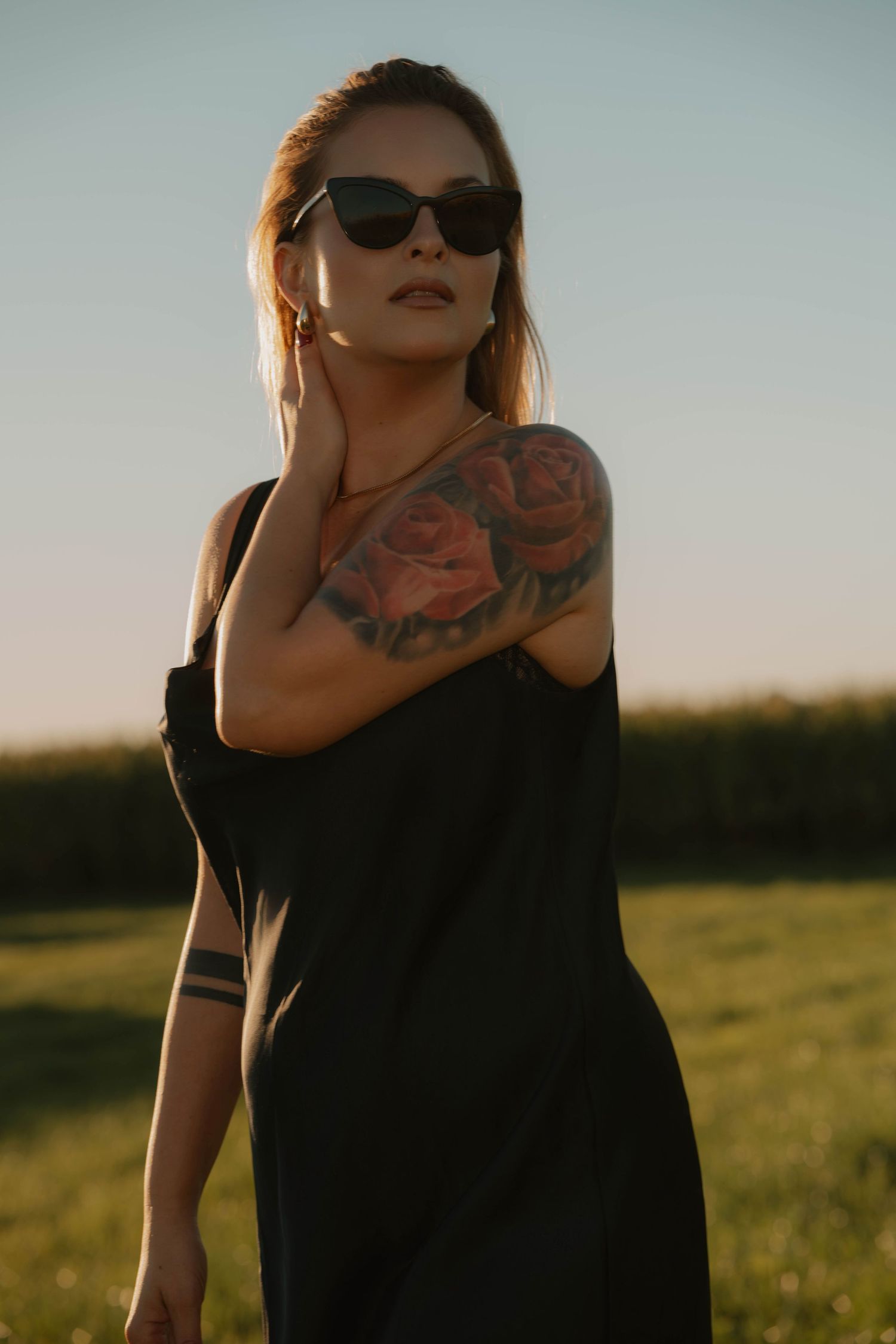 Artistic fashion portrait at sunset showing a figure in black against golden light wearing sunglasses.