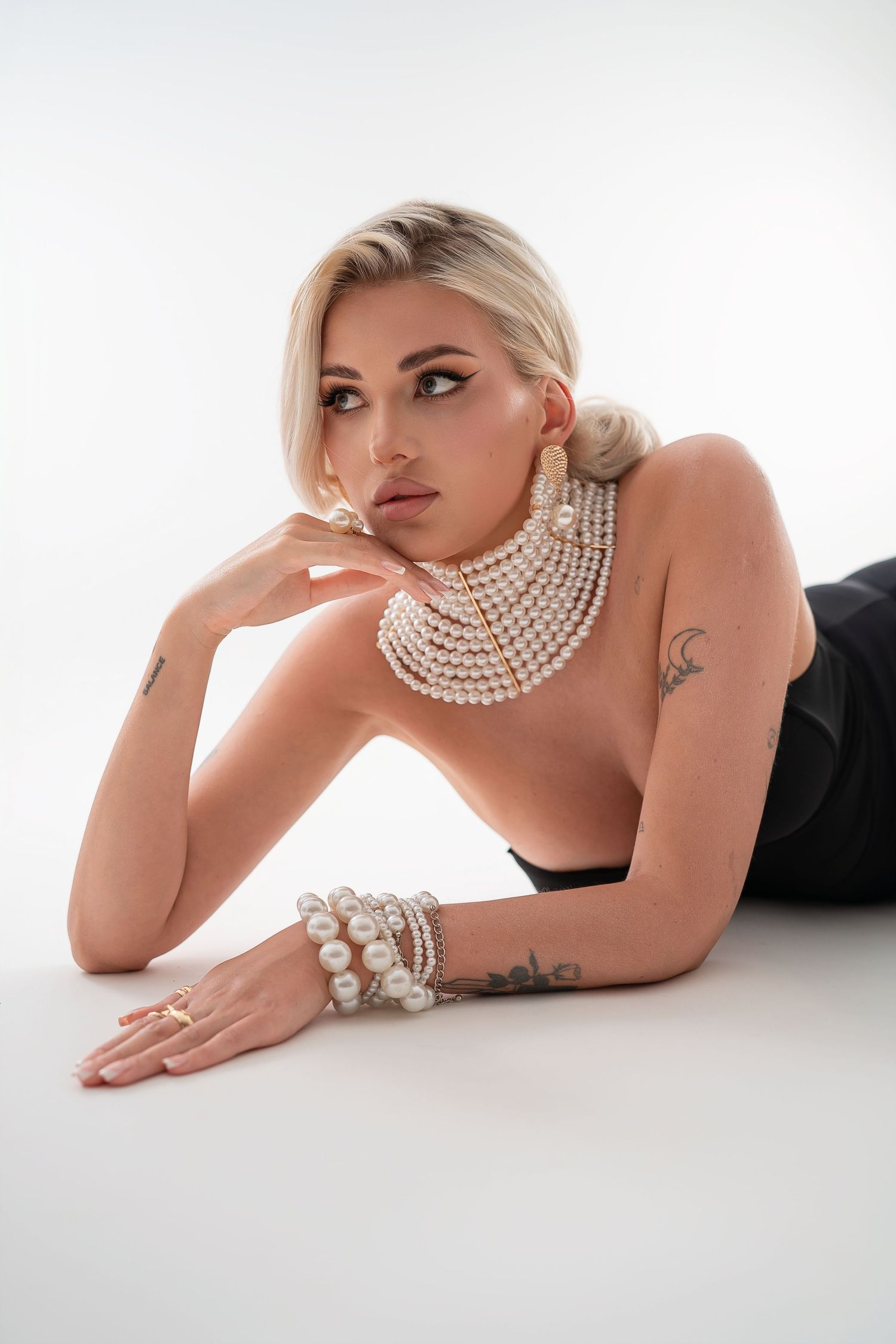 Fashion portrait featuring a striking look with layered pearl necklace and bracelets against white background.