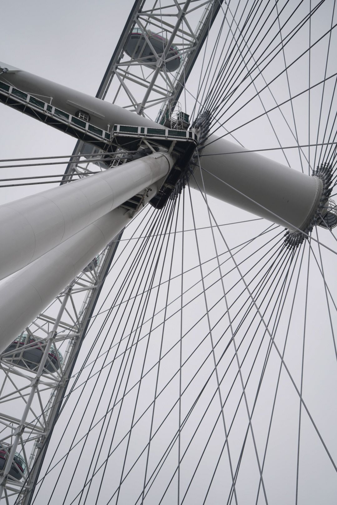Upward architectural view of the London Eye's geometric spokes and support structure against a grey sky.