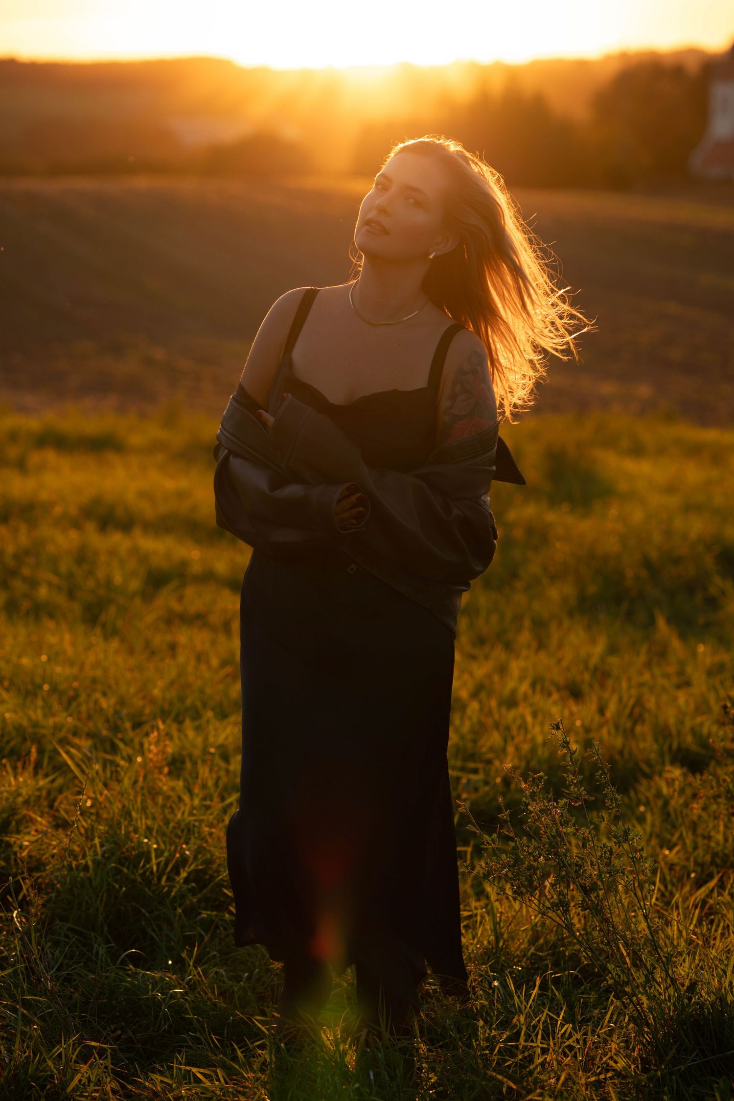 A silhouette stands in a golden field at sunset with long hair flowing in the breeze, creating a dreamy atmosphere.