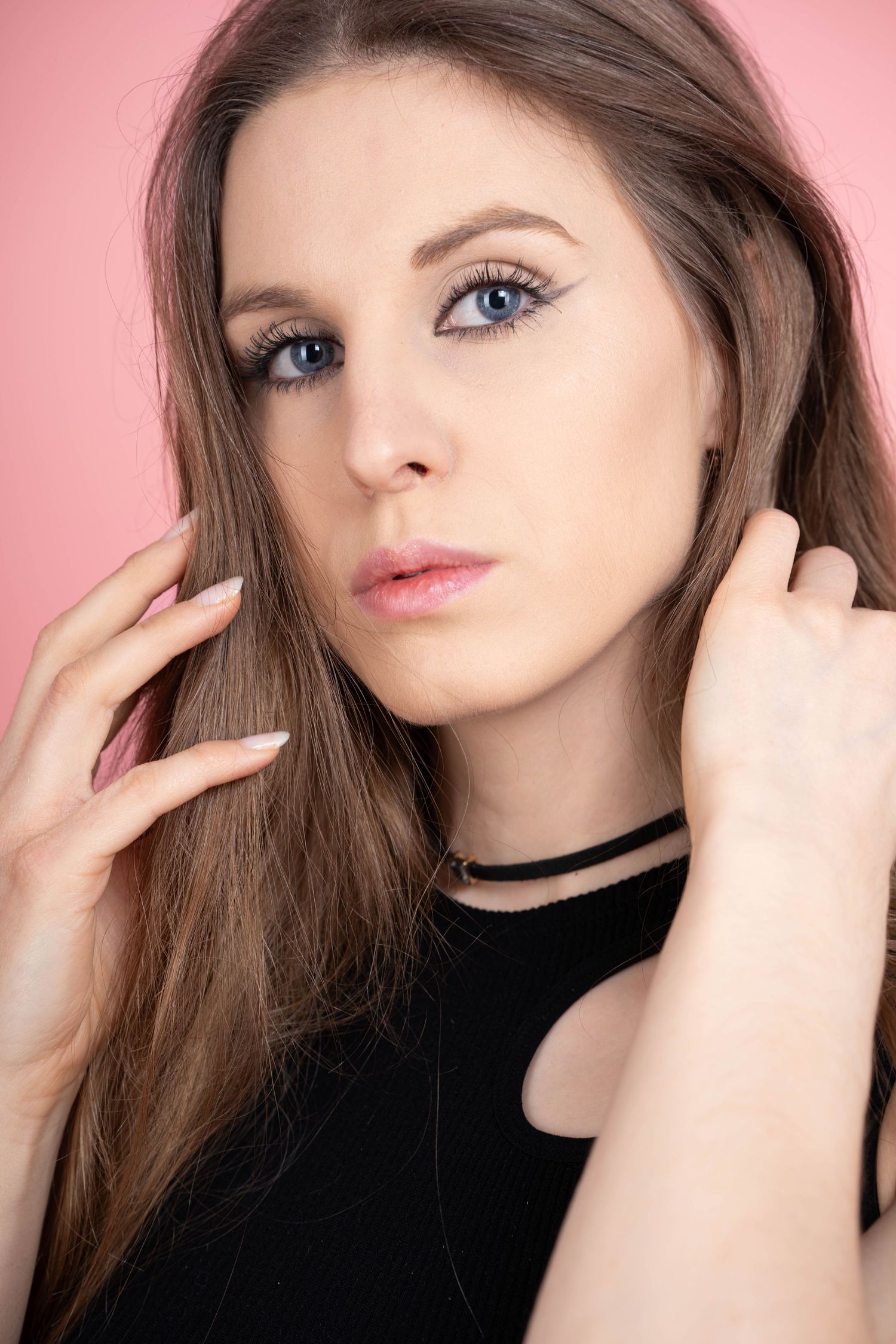 Beauty portrait against pink backdrop showcasing makeup and styled hair.