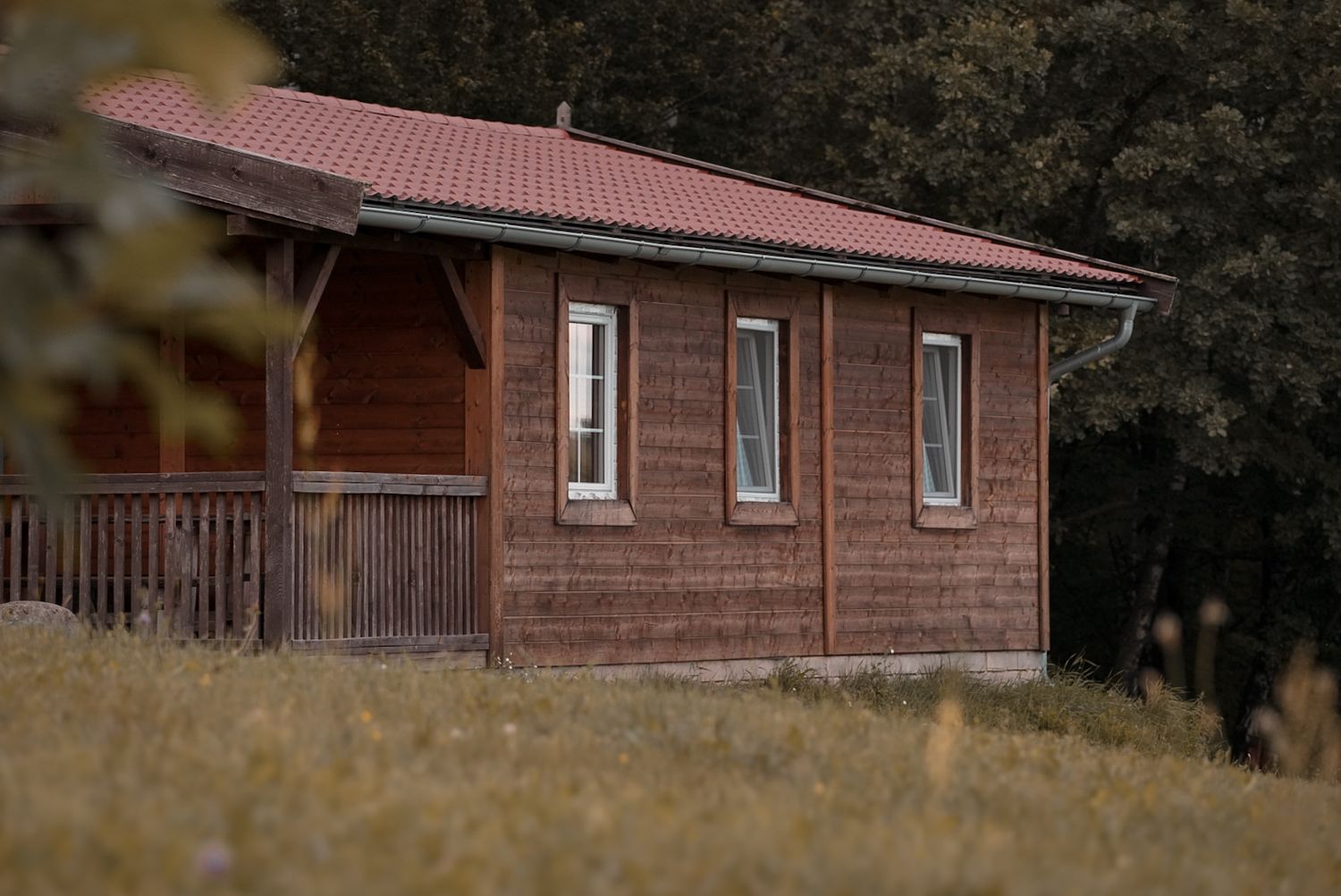 Small wooden cabin with red roof and three windows in a rural field setting.