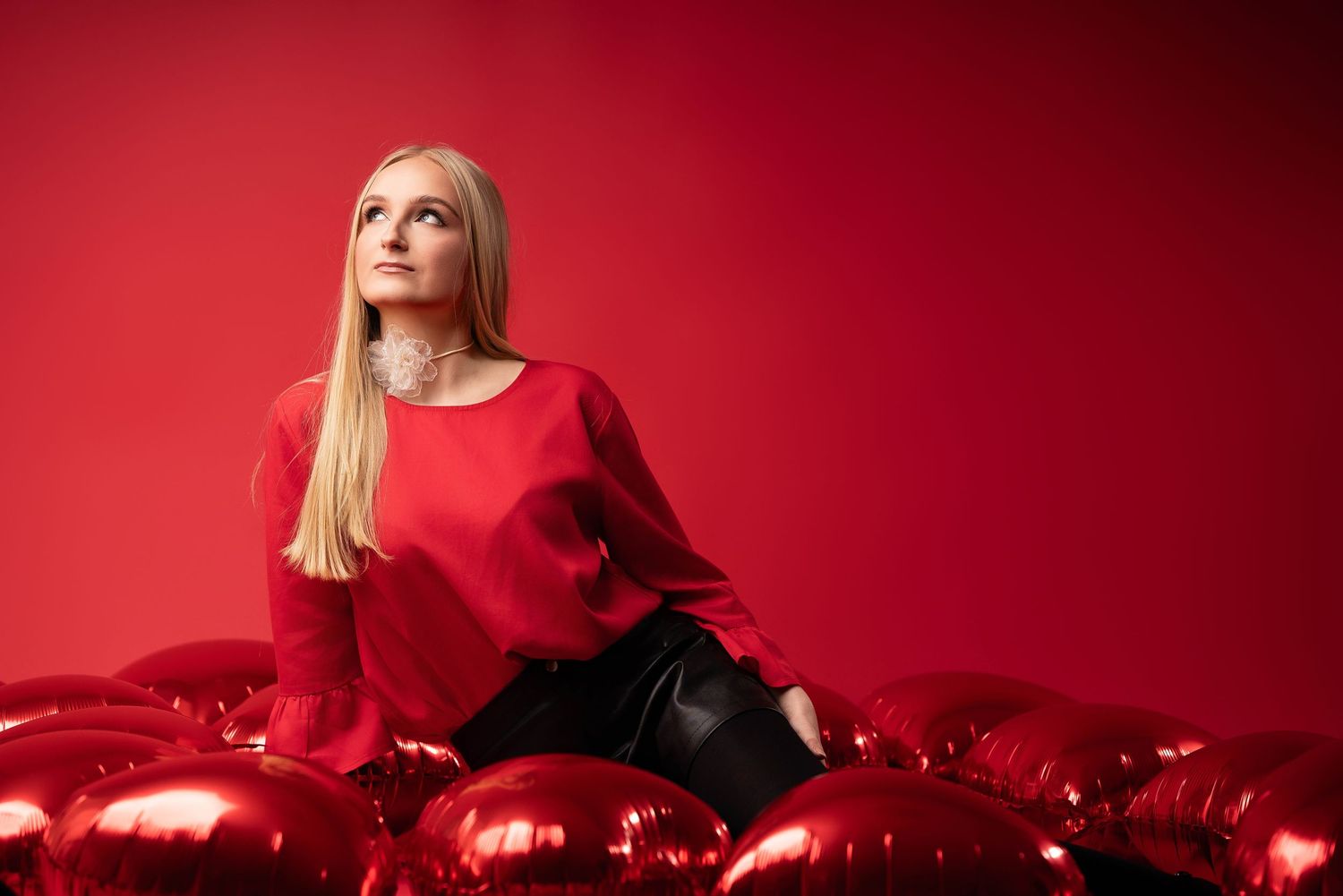 Woman in red dress poses against crimson background with shiny red Christmas ornaments and decorations.