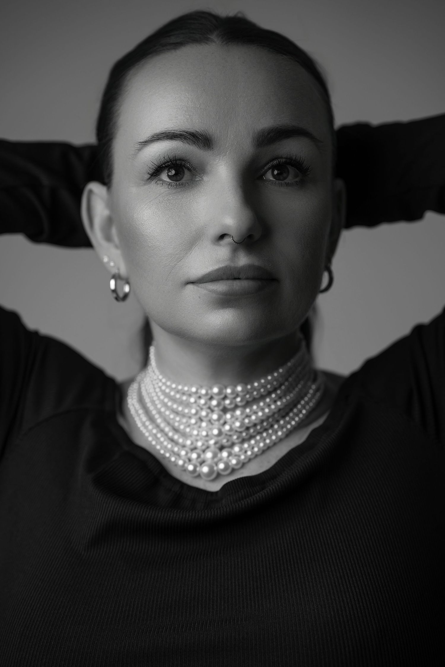 Black and white portrait series showing dramatic closeups of a face adorned with elegant pearl necklaces against dark background.